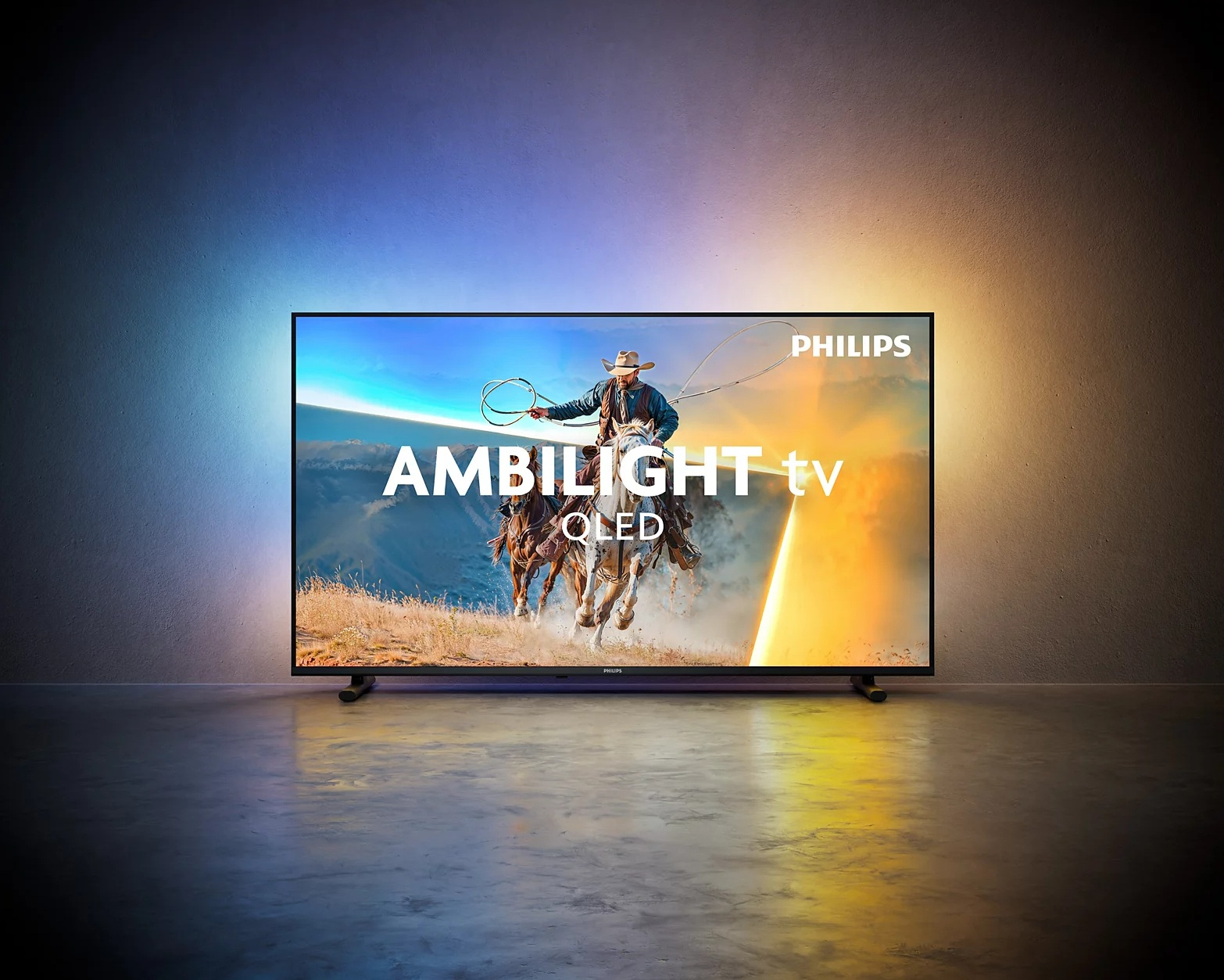Telewizor Philips Ambilight QLED stoi na podłodze pod ścianą z kolorowym podświetleniem.
