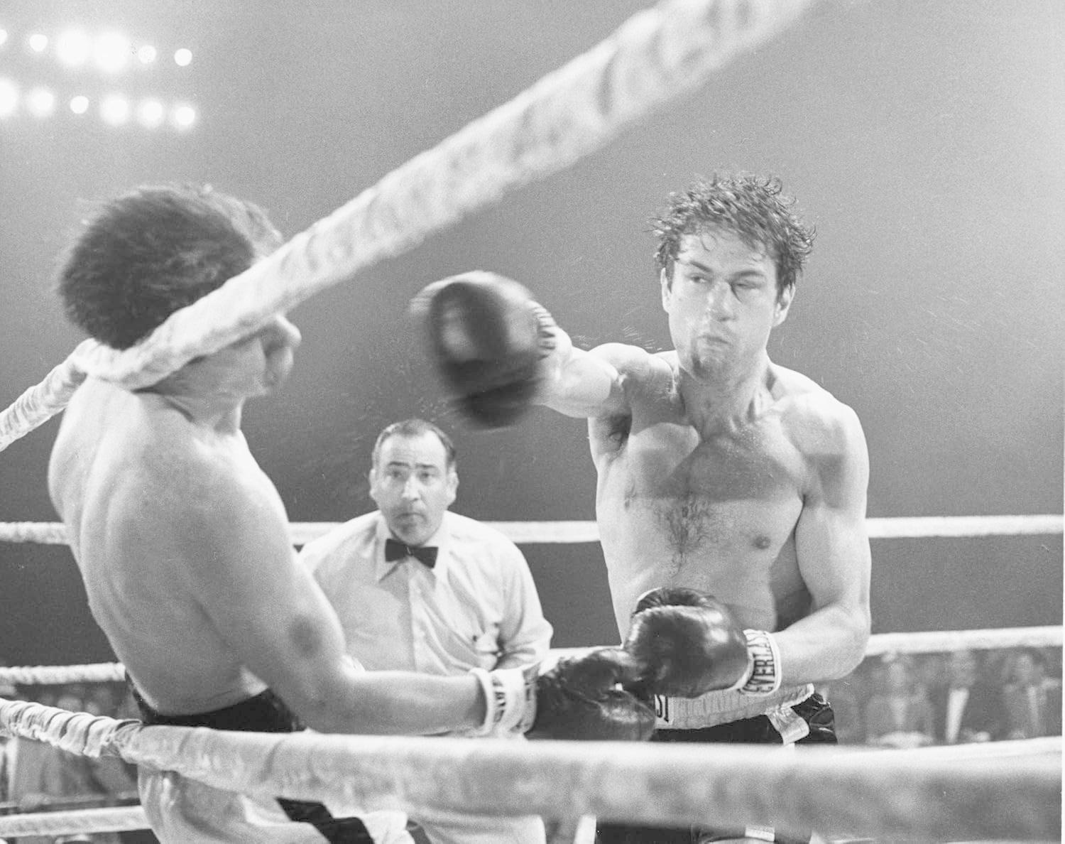 Ein Boxer schlägt im Ring einen Gegner, während ein Schiedsrichter zuschaut.
