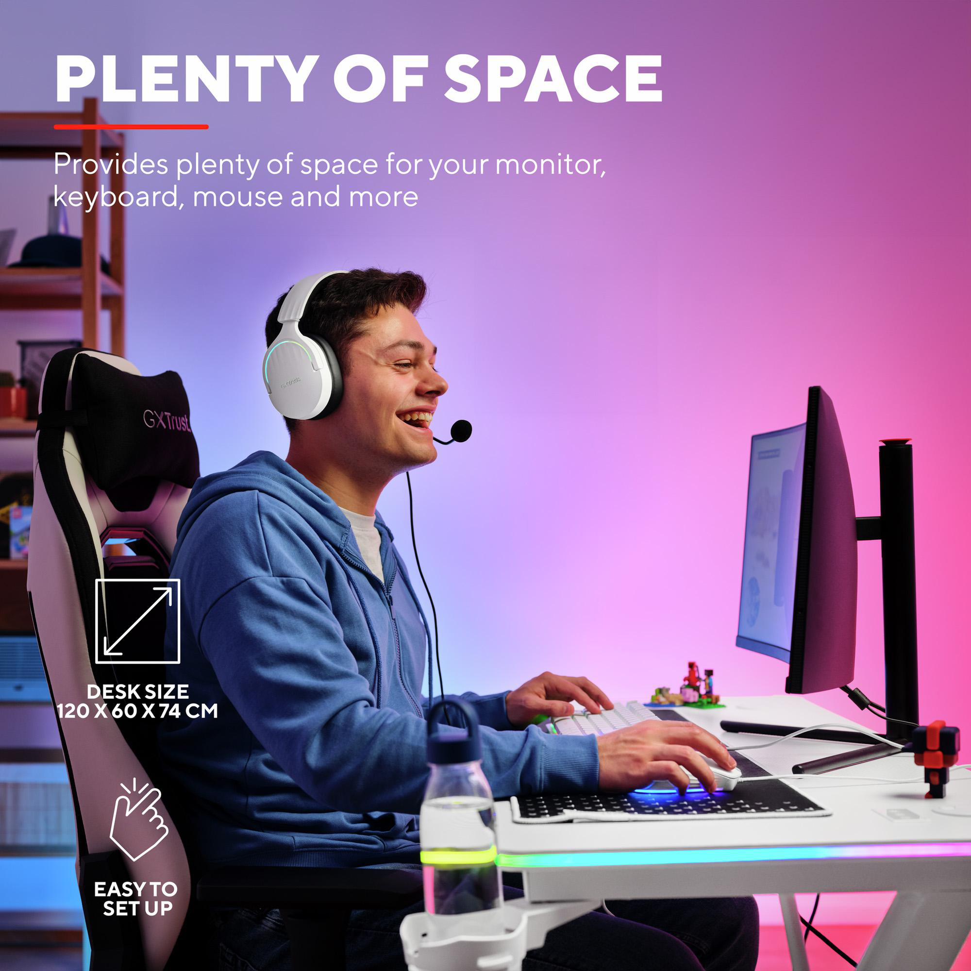 Junger Mann sitzt in einem blauen Pullover und mit Headset am beleuchteten Gaming-Schreibtisch.