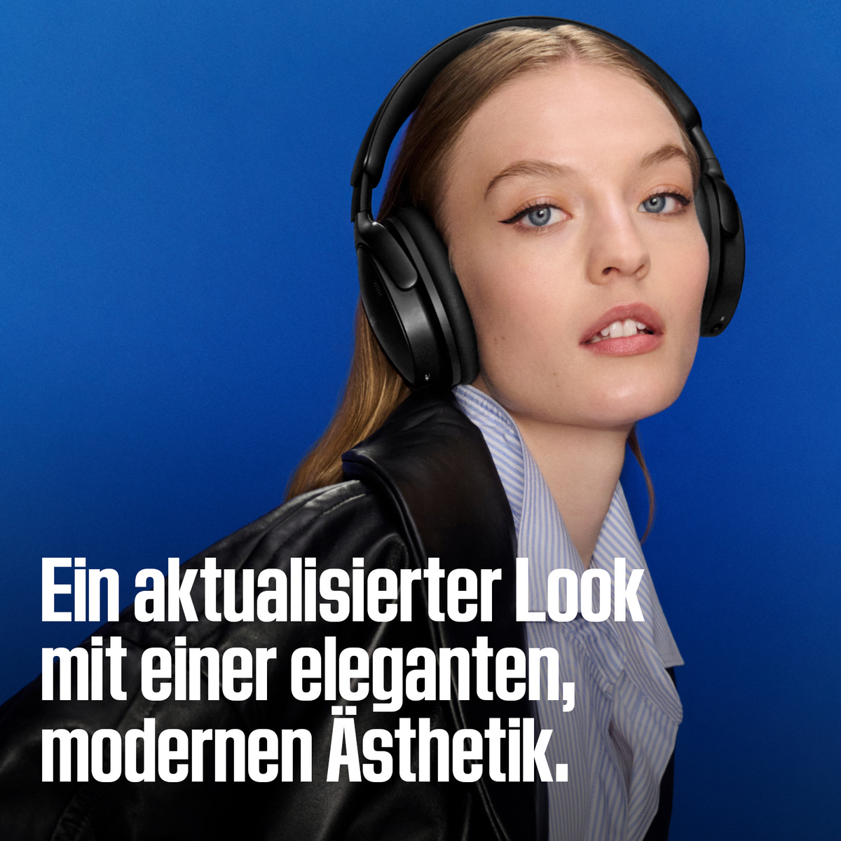 Eine Frau mit schwarzen Kopfhörern, einem gestreiften Hemd und einer Lederjacke vor blauem Hintergrund.