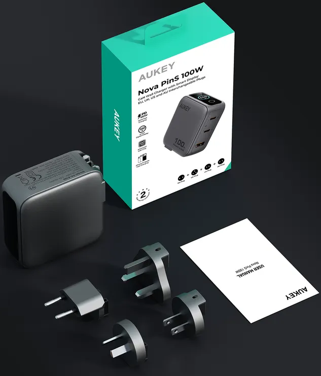 Aukey 100W GaN Wandladegerät mit Verpackung, vier Steckern und Anleitung auf dunklem Hintergrund.