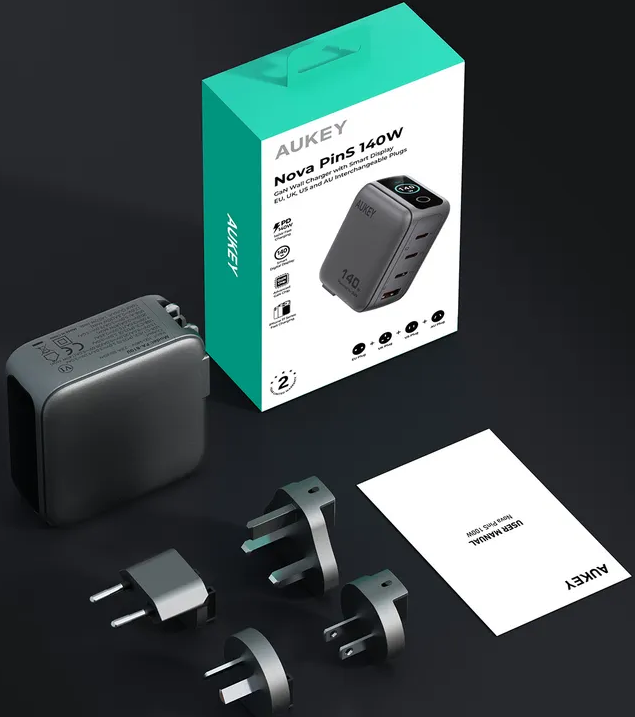 Ein graues Aukey Nova PinS 140W Ladegerät mit vier Steckern, Handbuch und türkiser Verpackung.
