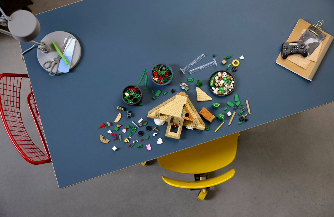 Lego-Pyramidenbau auf einem blauen Tisch mit Stühlen, Lampe und Notizbuch.
