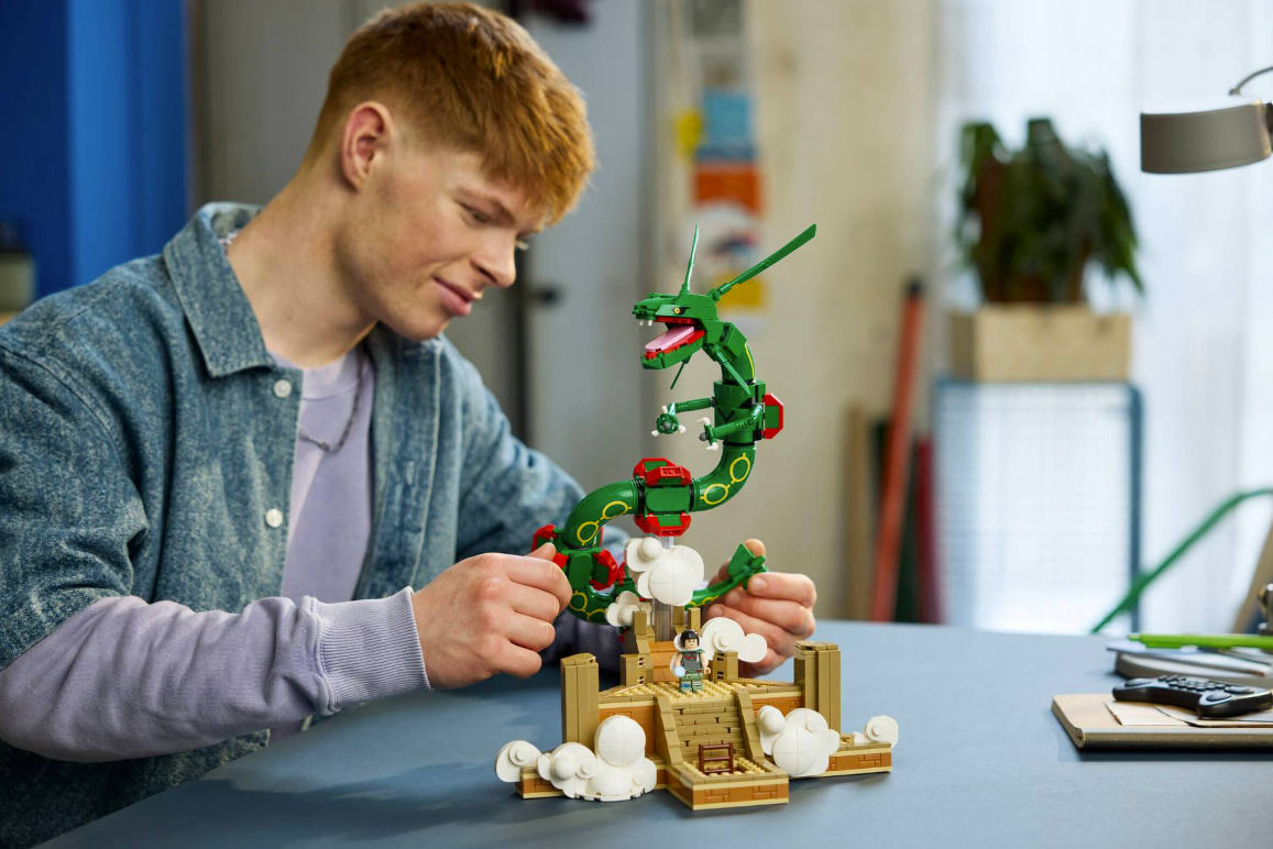 Ein junger Mann baut ein detailliertes grünes LEGO-Drachenmodell auf einem Schreibtisch.