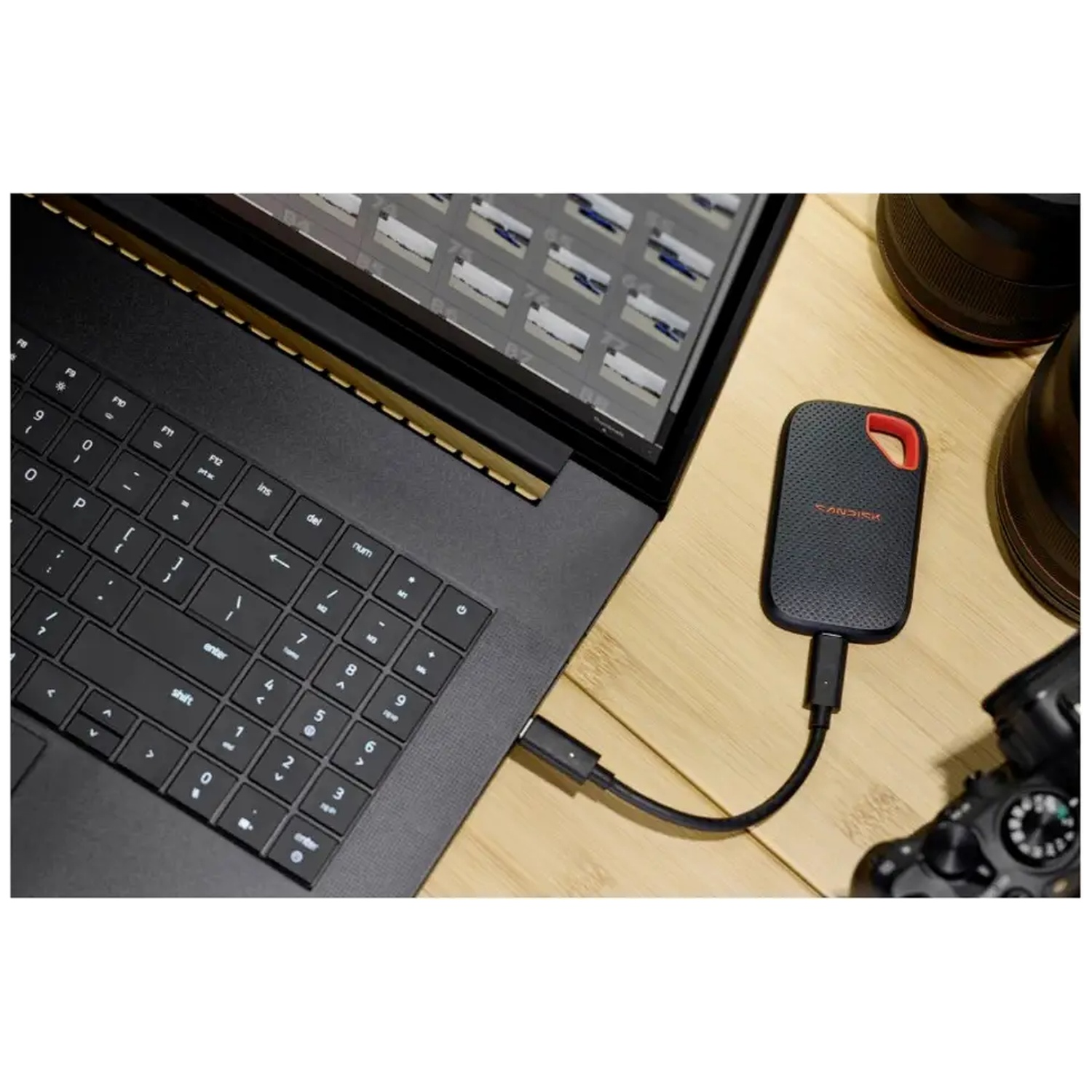 Un SSD portable SanDisk noir est connecté par un câble à un ordinateur portable sur un bureau en bois.