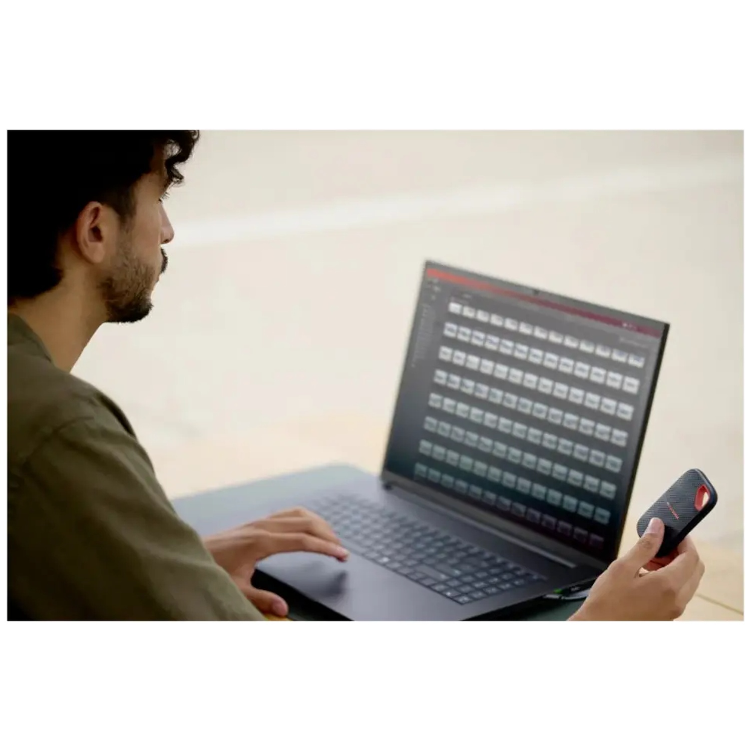 Un homme est assis devant un ordinateur portable et tient un petit appareil de stockage noir.