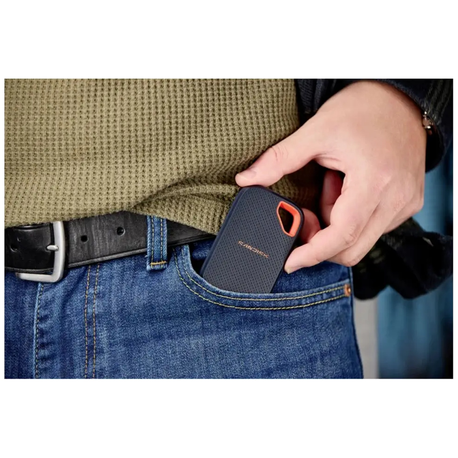Une personne met un SSD portable SanDisk bleu dans sa poche de jean.