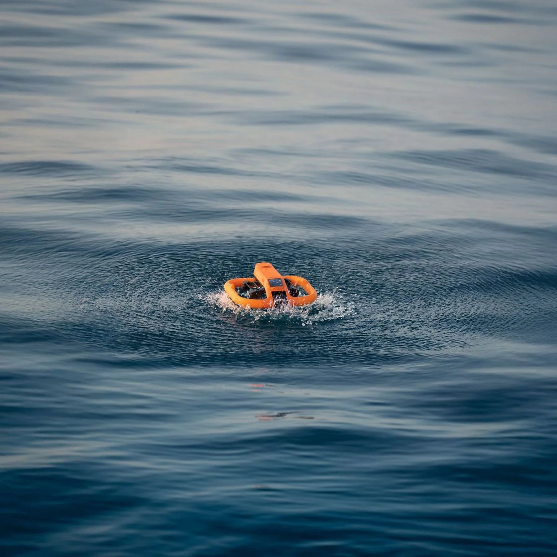 Un dispositivo submarino naranja flota en el mar azul y tranquilo, creando pequeñas ondas.