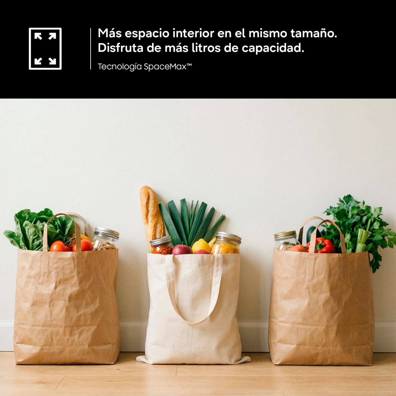Tres bolsas llenas de comestibles, incluyendo verduras frescas, pan y tarros, apoyadas en una pared sobre suelo de madera.
