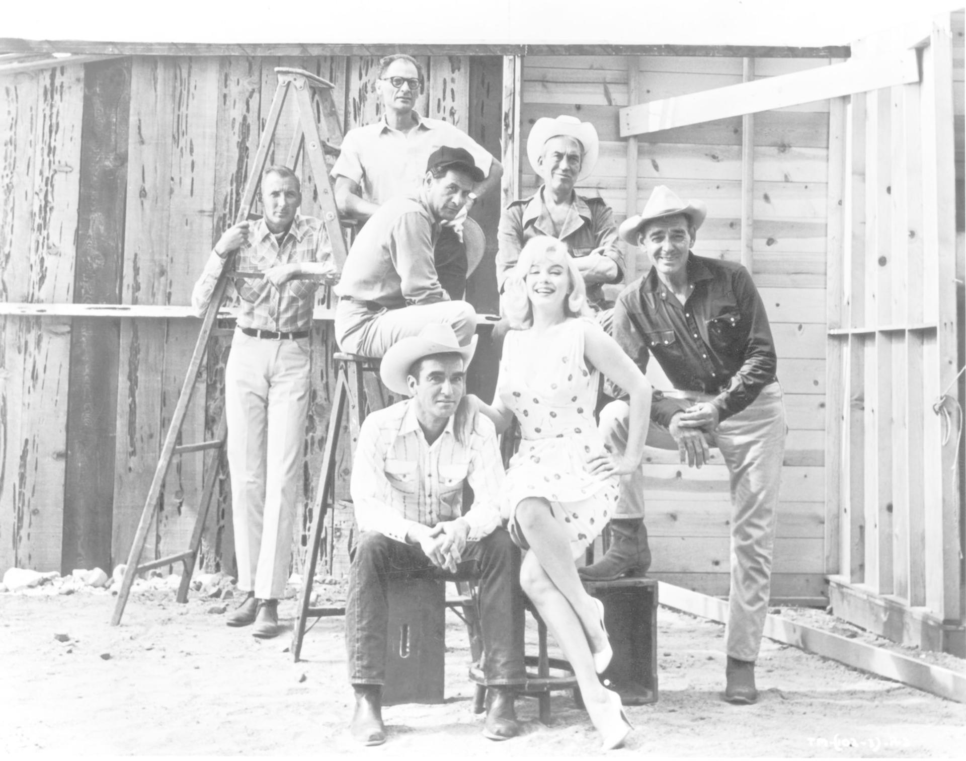 Marilyn Monroe und sechs Männer, darunter Clark Gable und Montgomery Clift, vor einer Holzwand.