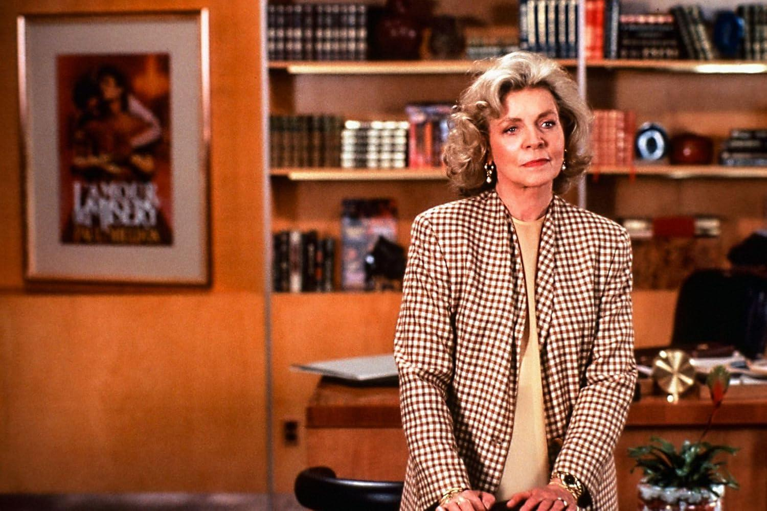 Eine blonde Frau im Karo-Blazer steht vor einem Bücherregal.