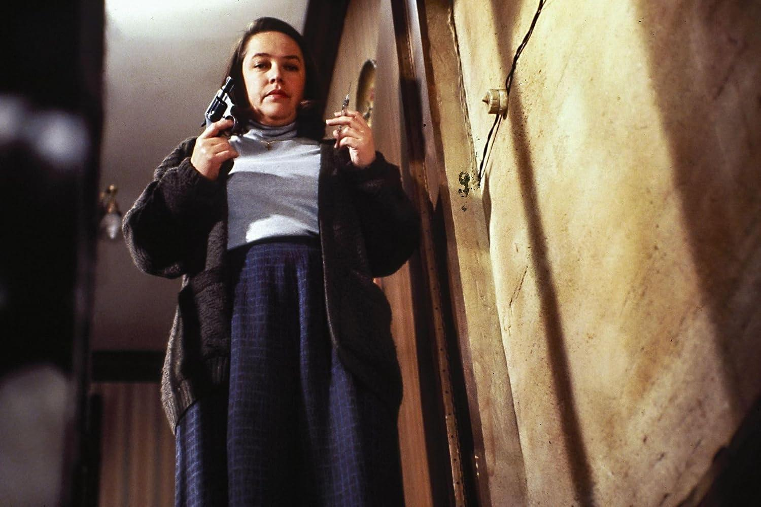 Eine Frau mit Waffe und Spritze steht in einem Flur vor einer Wand.