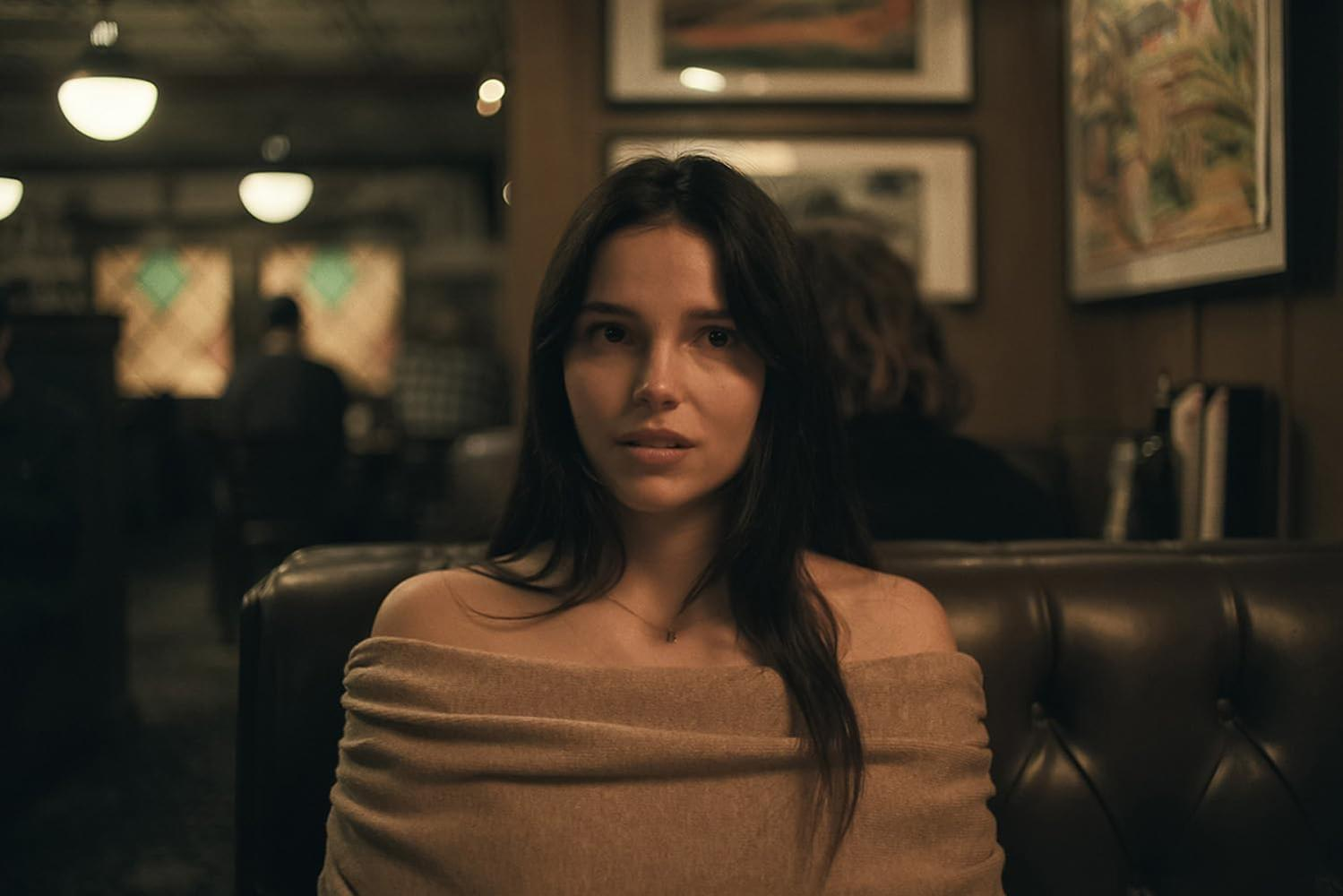 Eine Brünette im Off-Shoulder-Pullover sitzt in einem gemütlichen Restaurant.