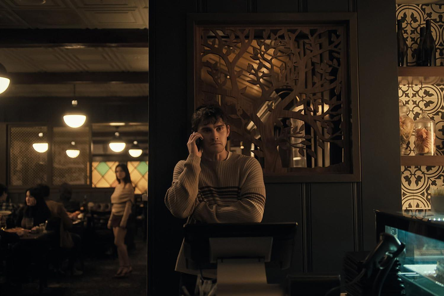Ein Mann in einem gestreiften Pullover telefoniert an der Theke eines gemütlichen Restaurants mit gedimmtem Licht.