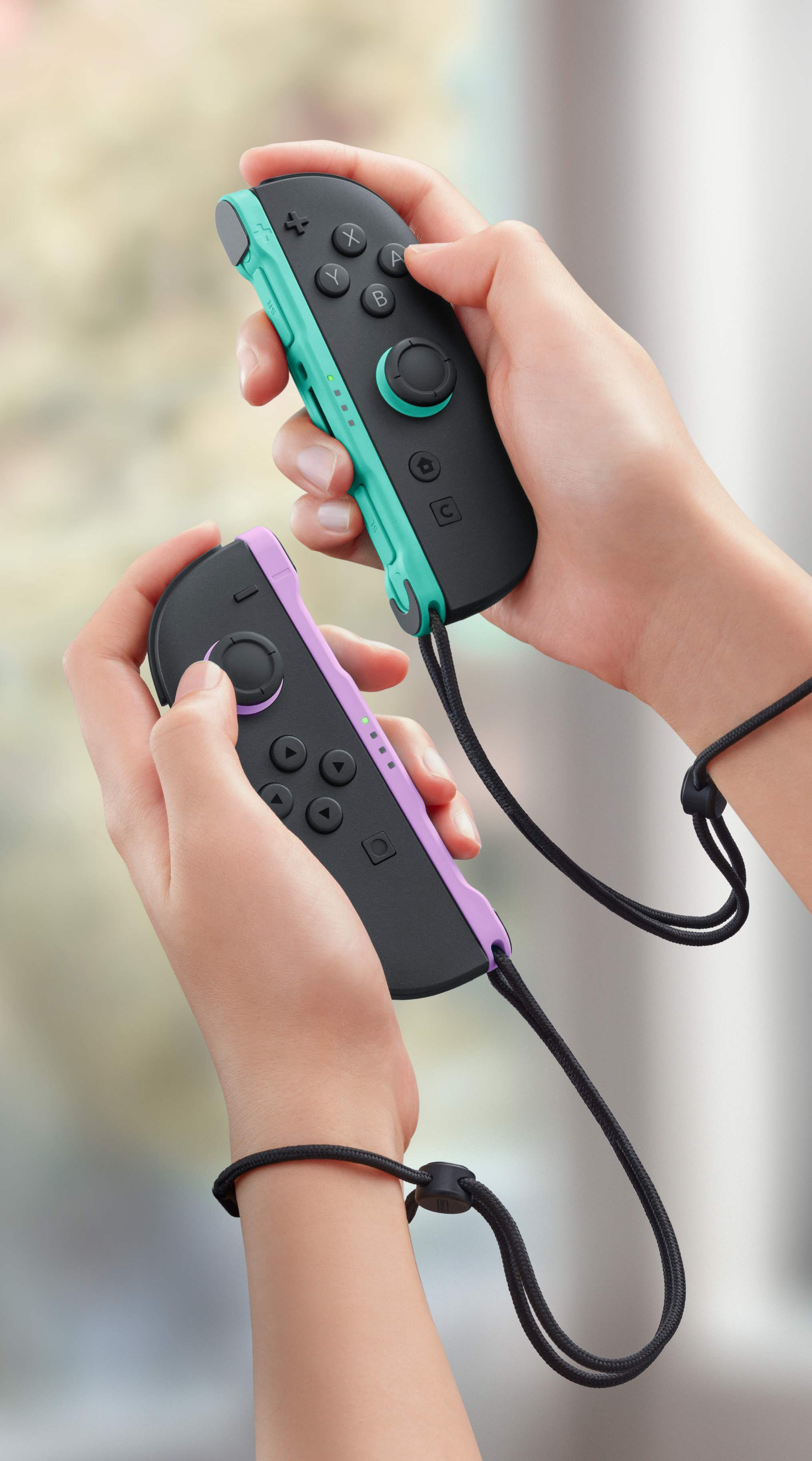 Osoba trzymająca dwa kolorowe kontrolery Joy-Con w czarnych etui ochronnych i z paskami na nadgarstek.