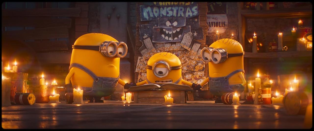 Drei gelbe Minions in blauen Latzhosen lesen ein Buch, umgeben von Kerzen.