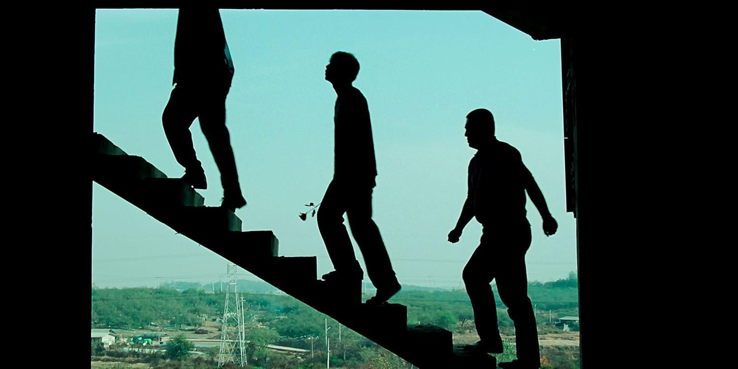 Drei männliche Silhouetten gehen im Gegenlicht Treppen hinauf, mit einem ländlichen Hintergrund.
