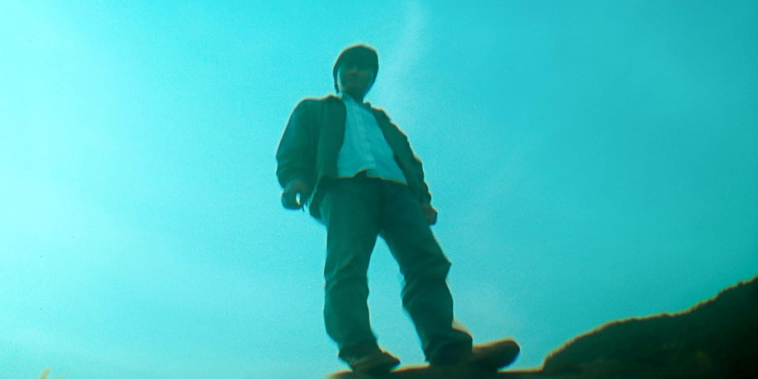 Ein Mensch in Jacke und Mütze steht draußen unter blauem Himmel und schaut nach unten.
