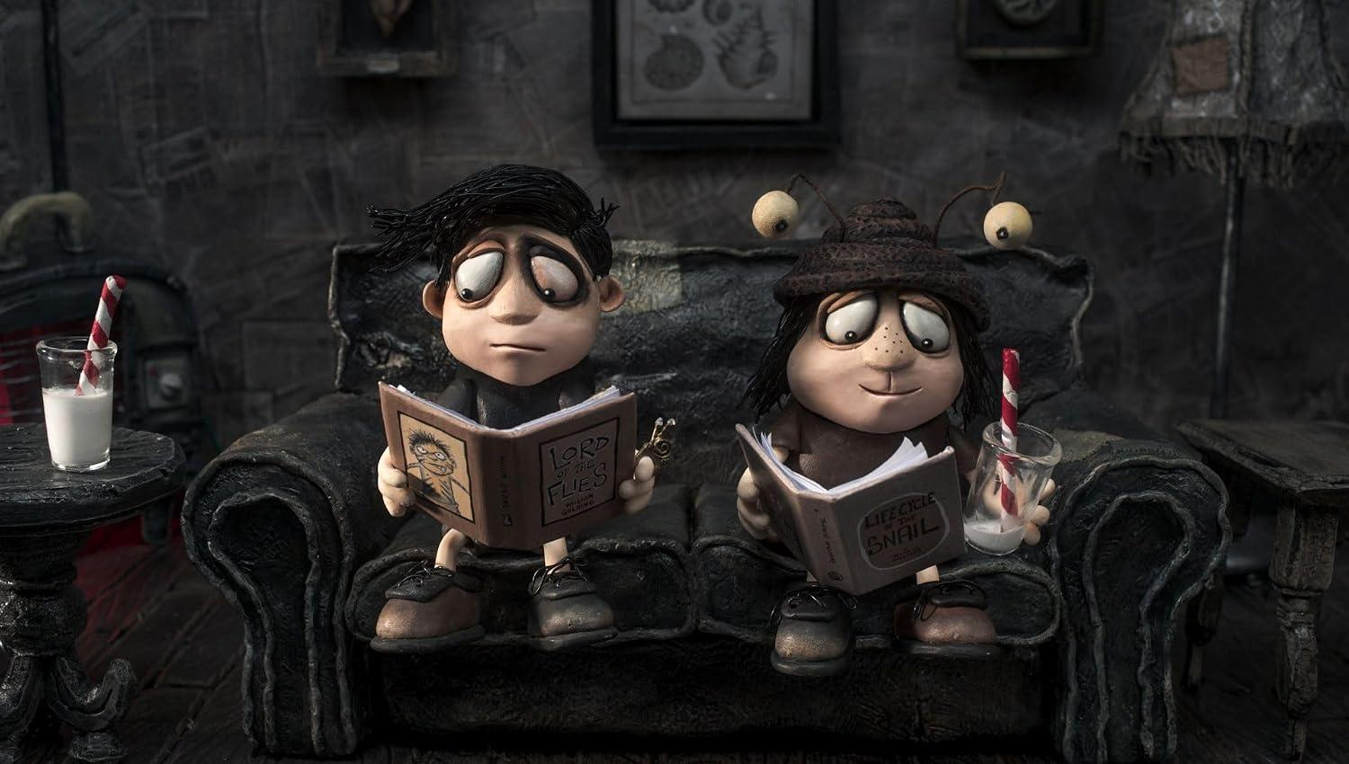 Zwei Stop-Motion-Puppen sitzen auf einer dunklen Couch und lesen Bücher, daneben Gläser mit Milch.