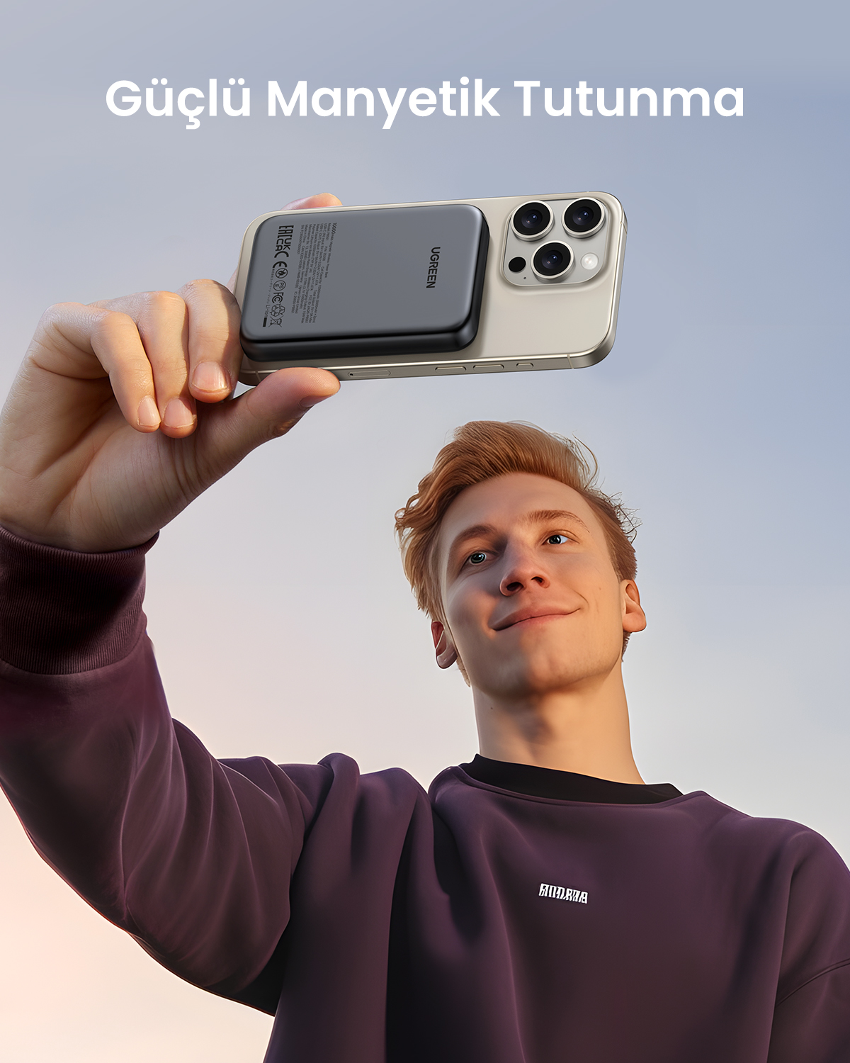 Genç bir adam, arkasında siyah Ugreen taşınmaz şarj cihazı olan bir akıllı telefonu yukarıda tutuyor.