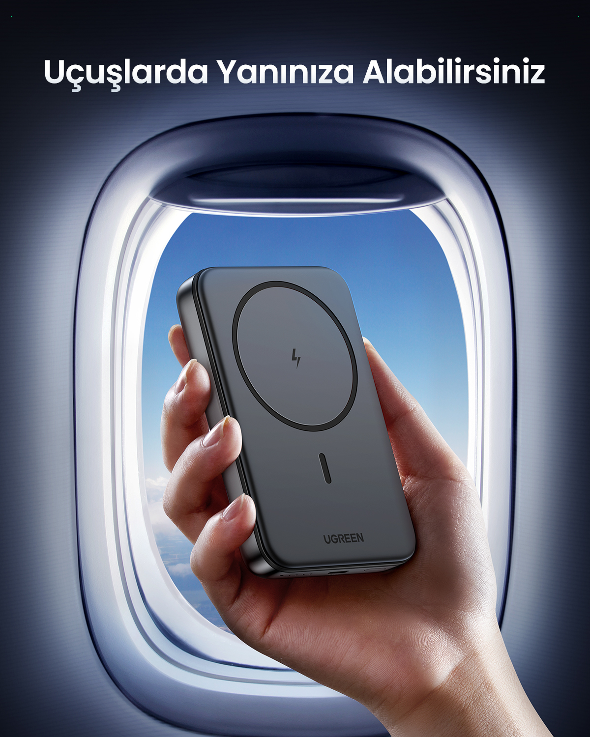 Bir el, mavi gökyüzü olan uçak penceresi önünde siyah Ugreen powerbank tutuyor.