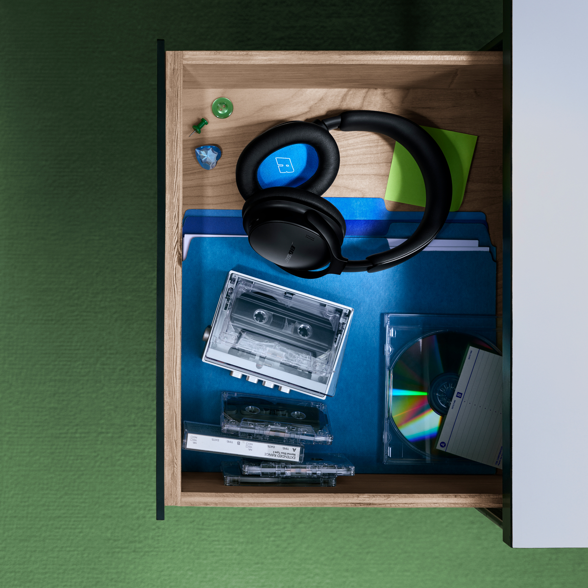 Eine geöffnete Schublade mit Kopfhörern, blauen Ordnern, Audiokassetten, einer CD und kleinen Büroklammern.