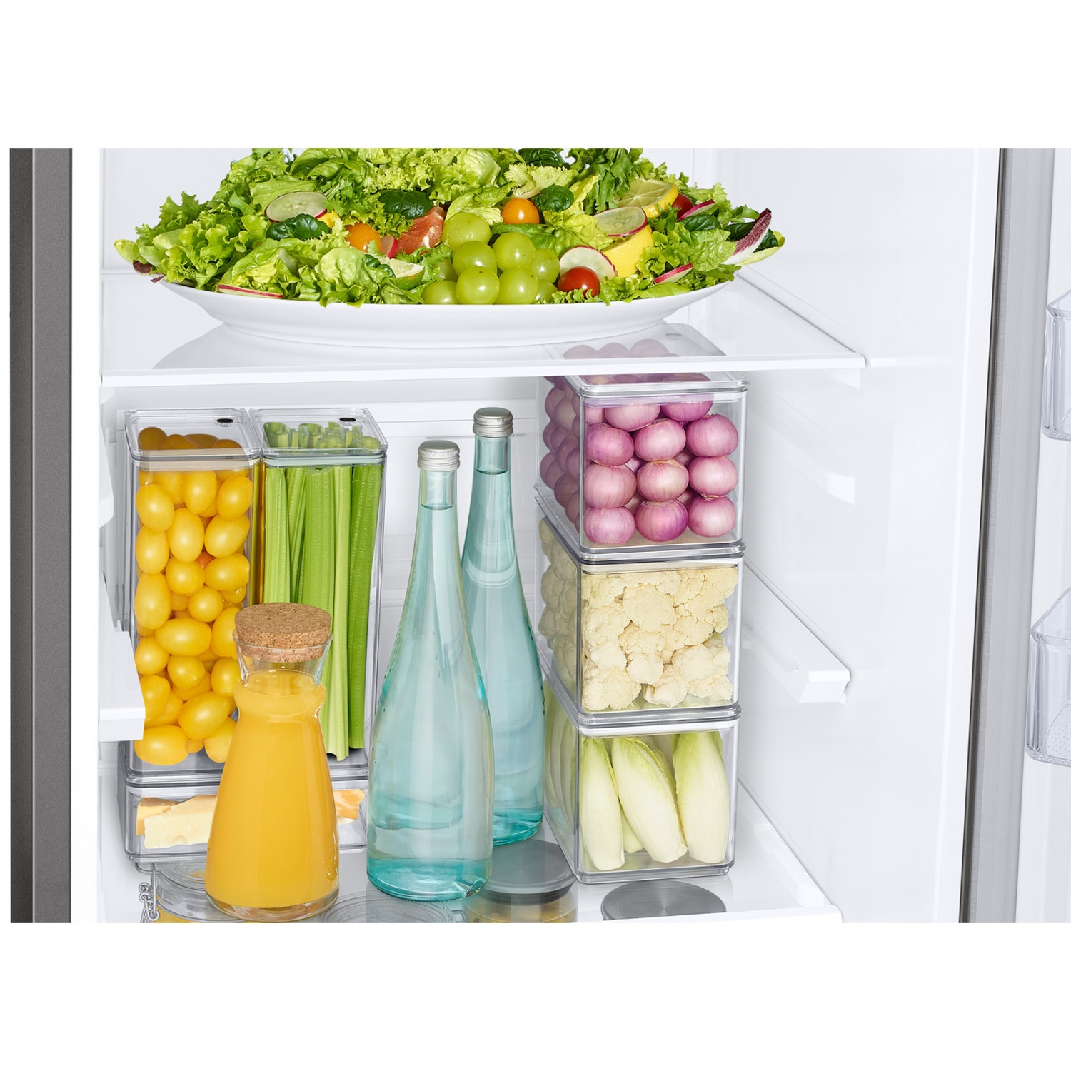 Koelkastinterieur gevuld met georganiseerde groenten, salade, sinaasappelsap en glazen flessen.