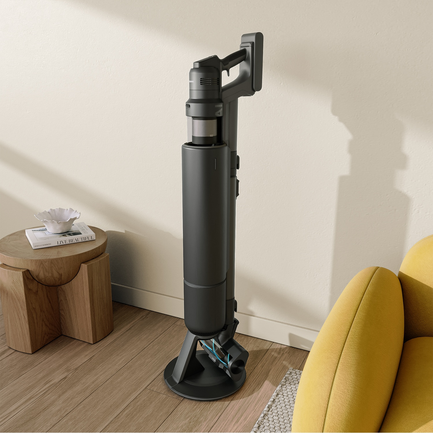 Een zwarte snoerloze stofzuiger staat rechtop op het oplaadstation in een kamer met een houten vloer en een gele fauteuil.