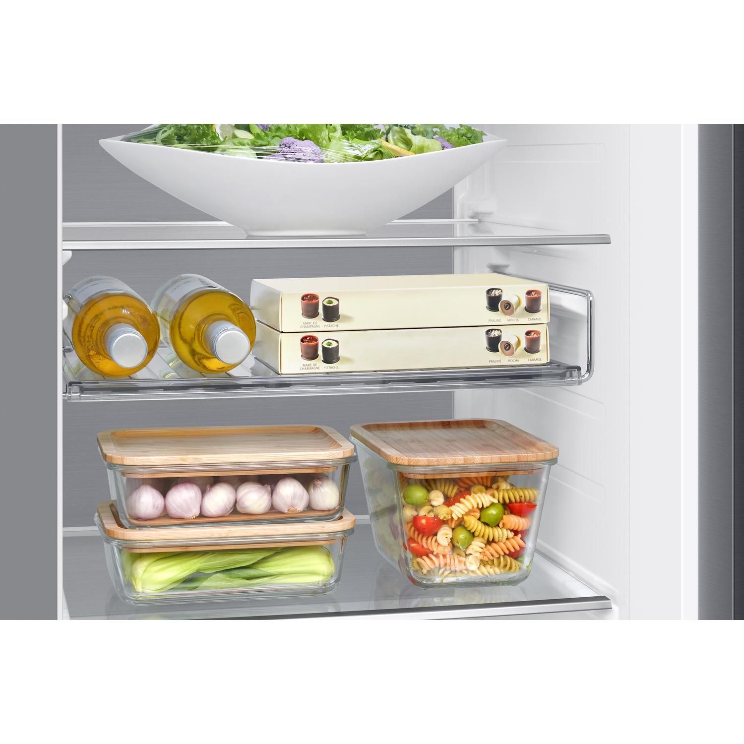 Un réfrigérateur bien rangé avec de la salade, des bouteilles, des boîtes et des récipients en verre de légumes et pâtes.