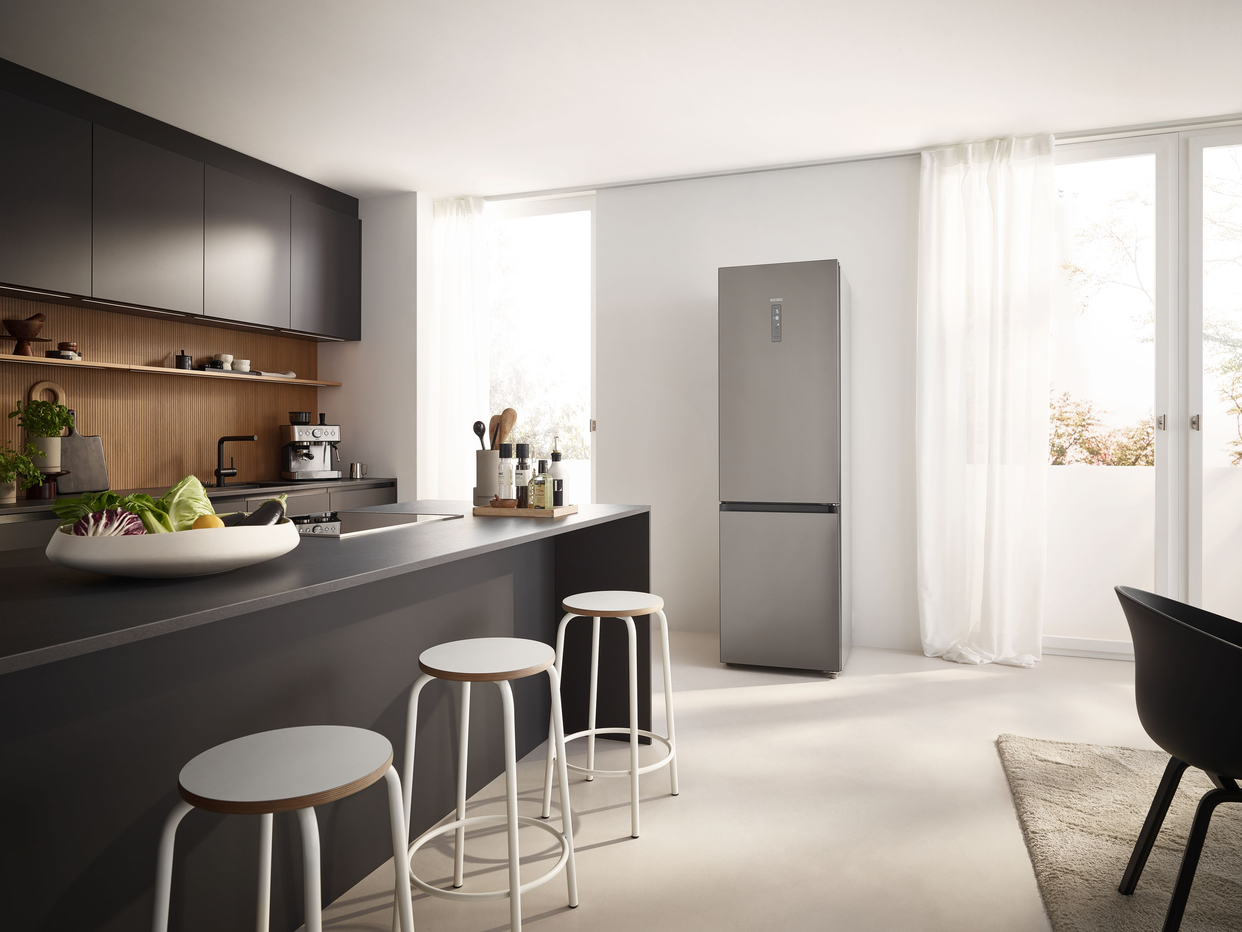 Moderne Küche mit schwarzer Kochinsel, weißen Barhockern, grauem Kühlschrank und großen Fenstern mit weißem Vorhang.