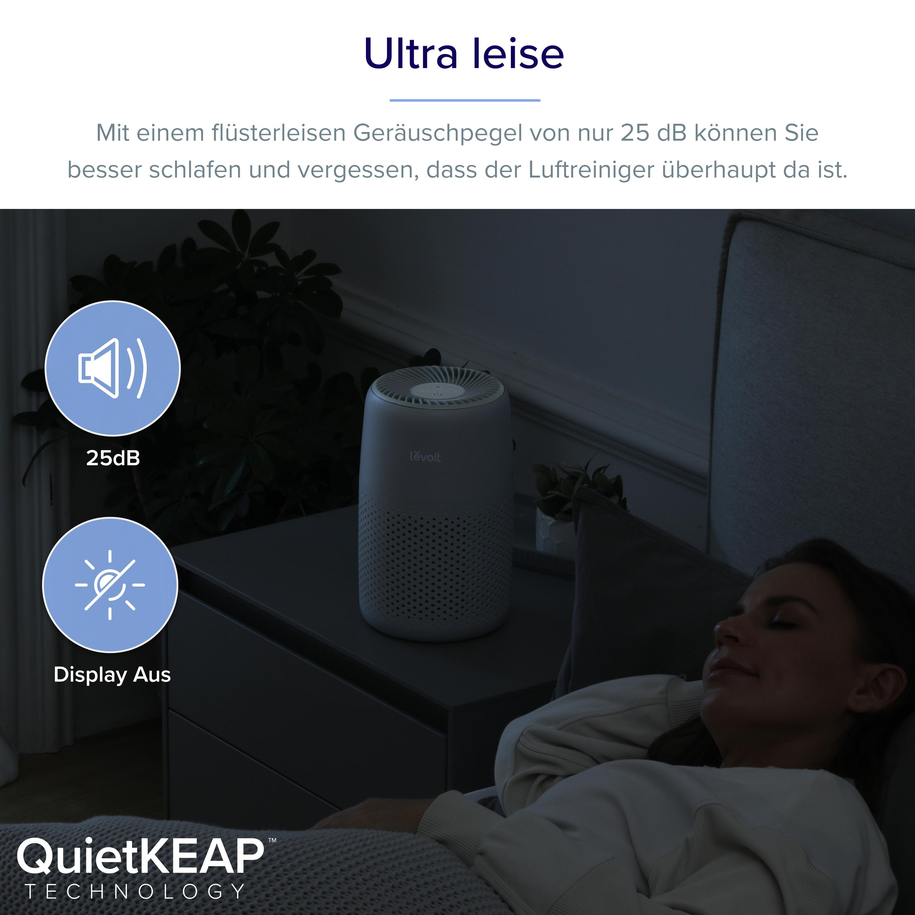 Ein weißer Luftreiniger steht auf einem Nachttisch, während eine Frau ruhig im Bett schläft.