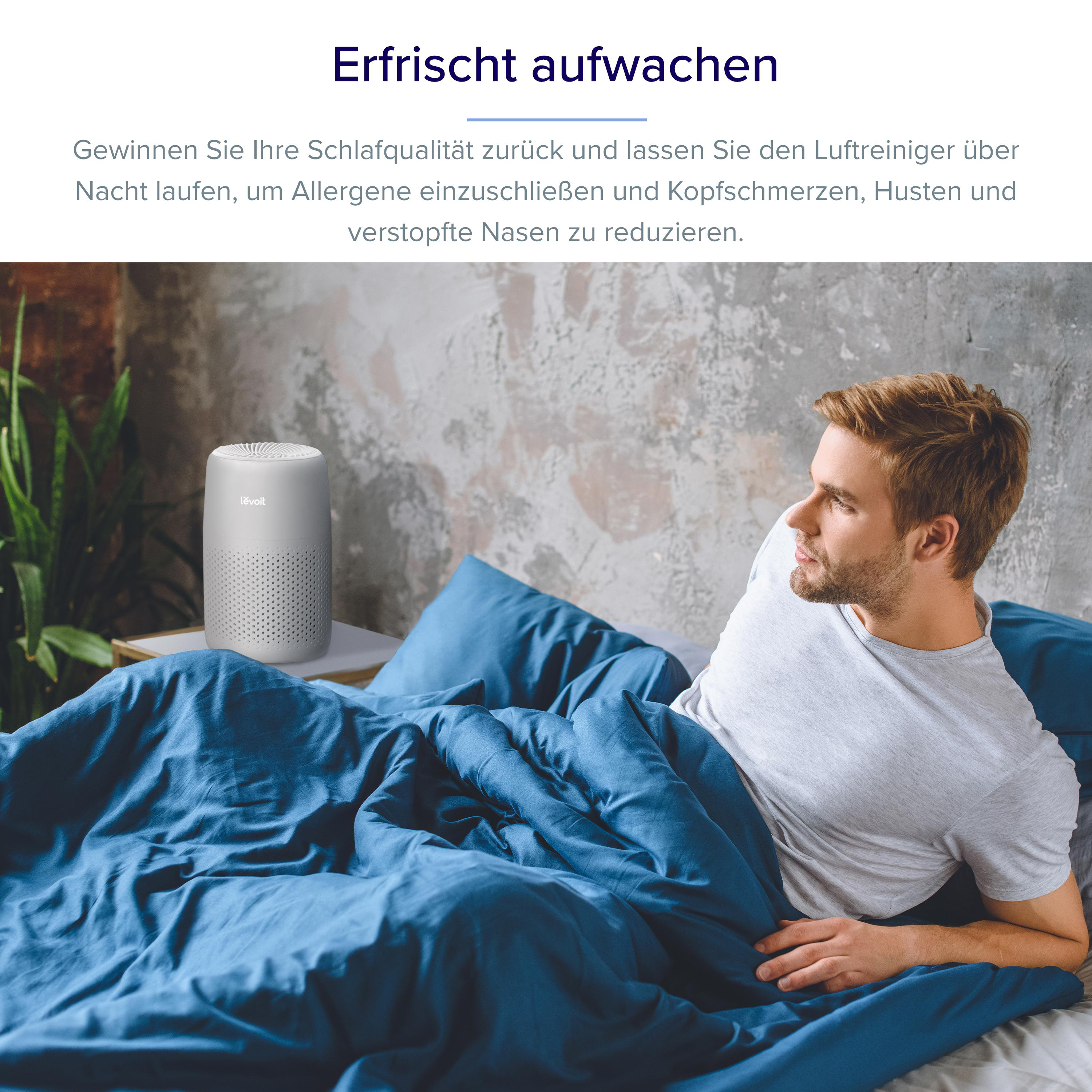 Ein Mann liegt morgens im blauen Bett, daneben steht ein Luftreiniger.