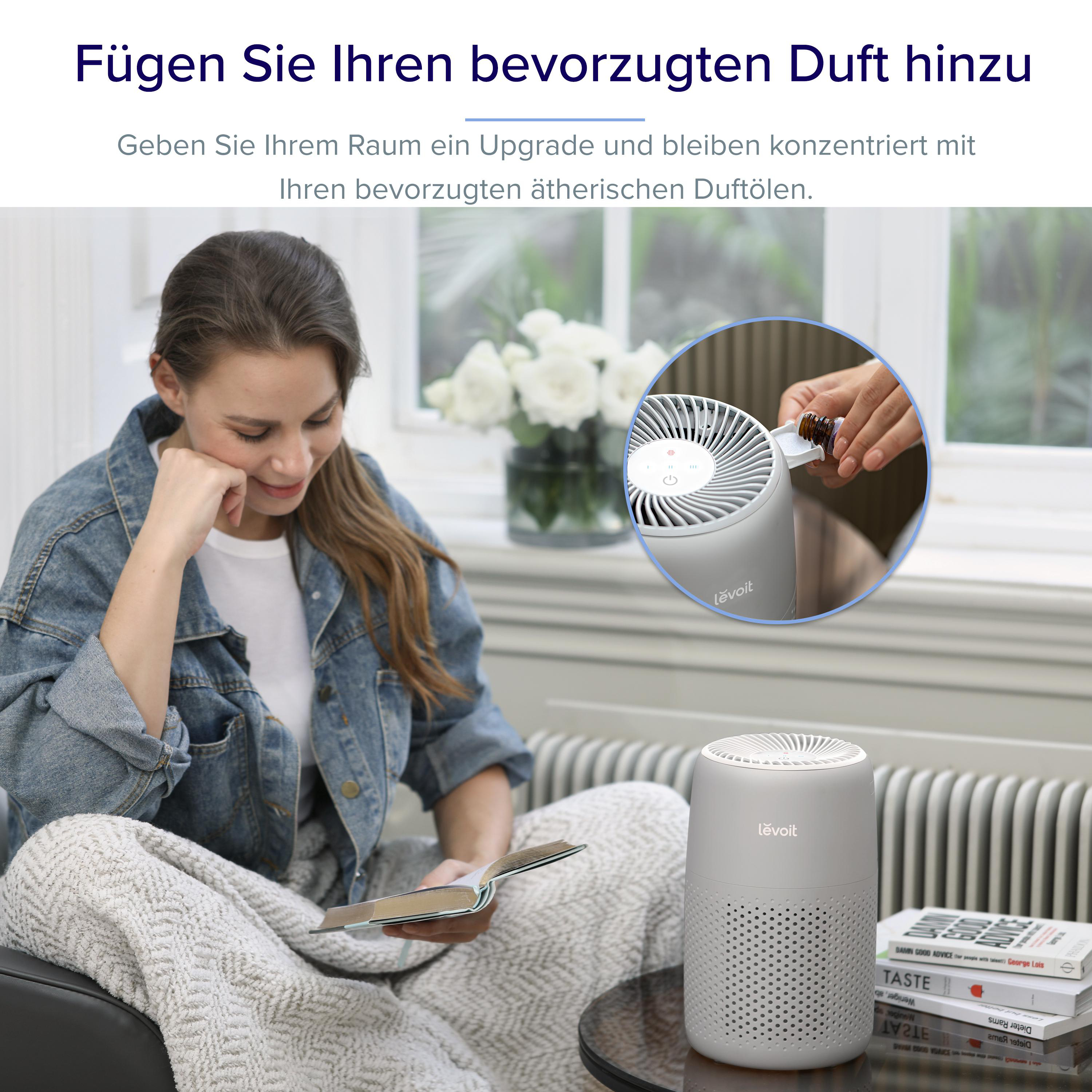 Eine Frau liest ein Buch auf einem Sofa neben einem Levoit Luftreiniger.