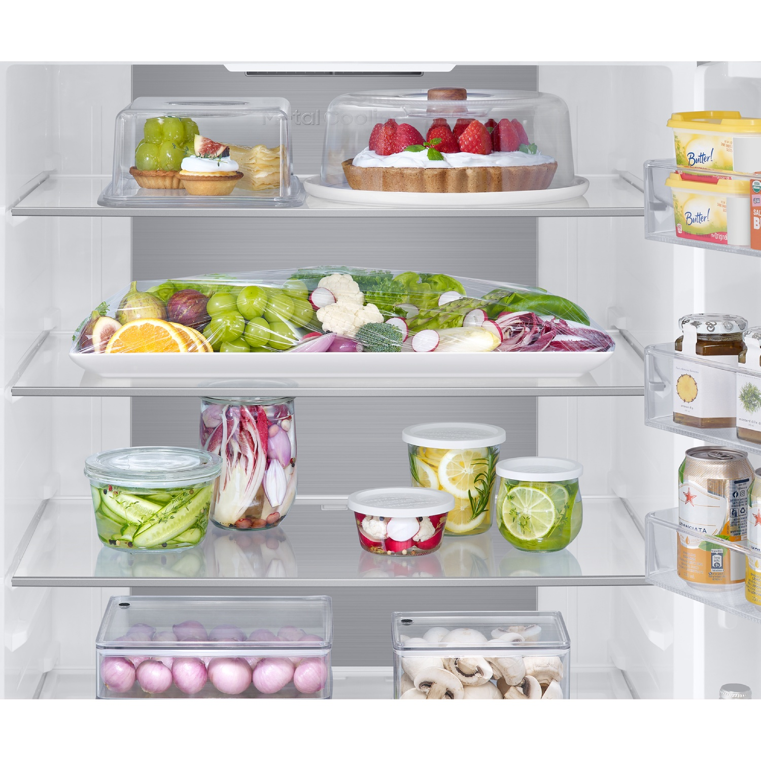 Un refrigerador limpio lleno de frutas frescas, verduras, pastel, frascos y mantequilla en la puerta.