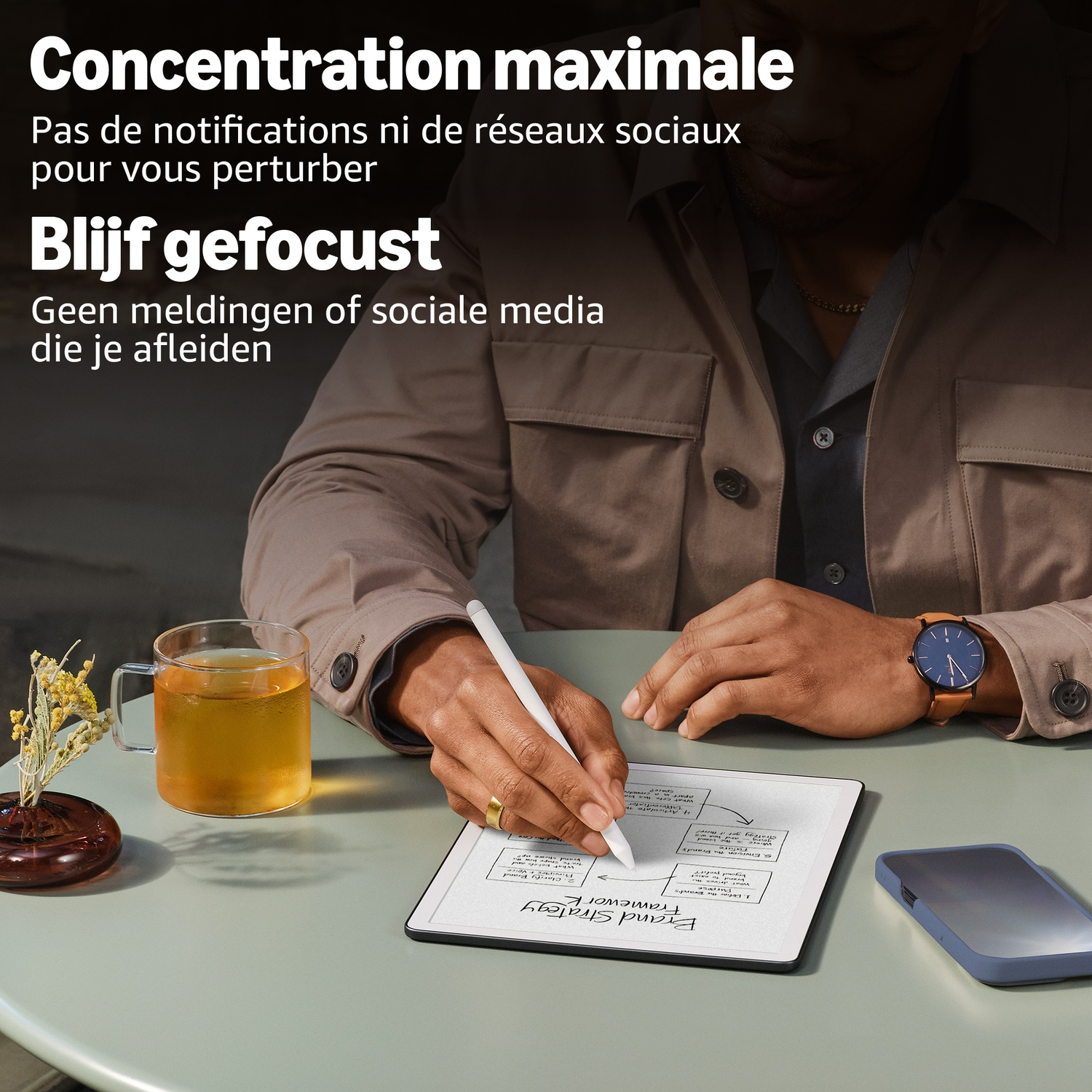Een man schrijft op een digitale tablet aan een bureau, met een glas thee en een smartphone.