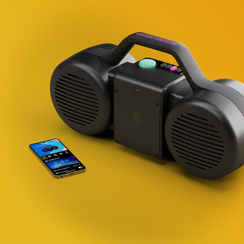Ein schwarzer Ghettoblaster mit Lautsprechern und ein Smartphone mit App liegen auf einer gelben Oberfläche.