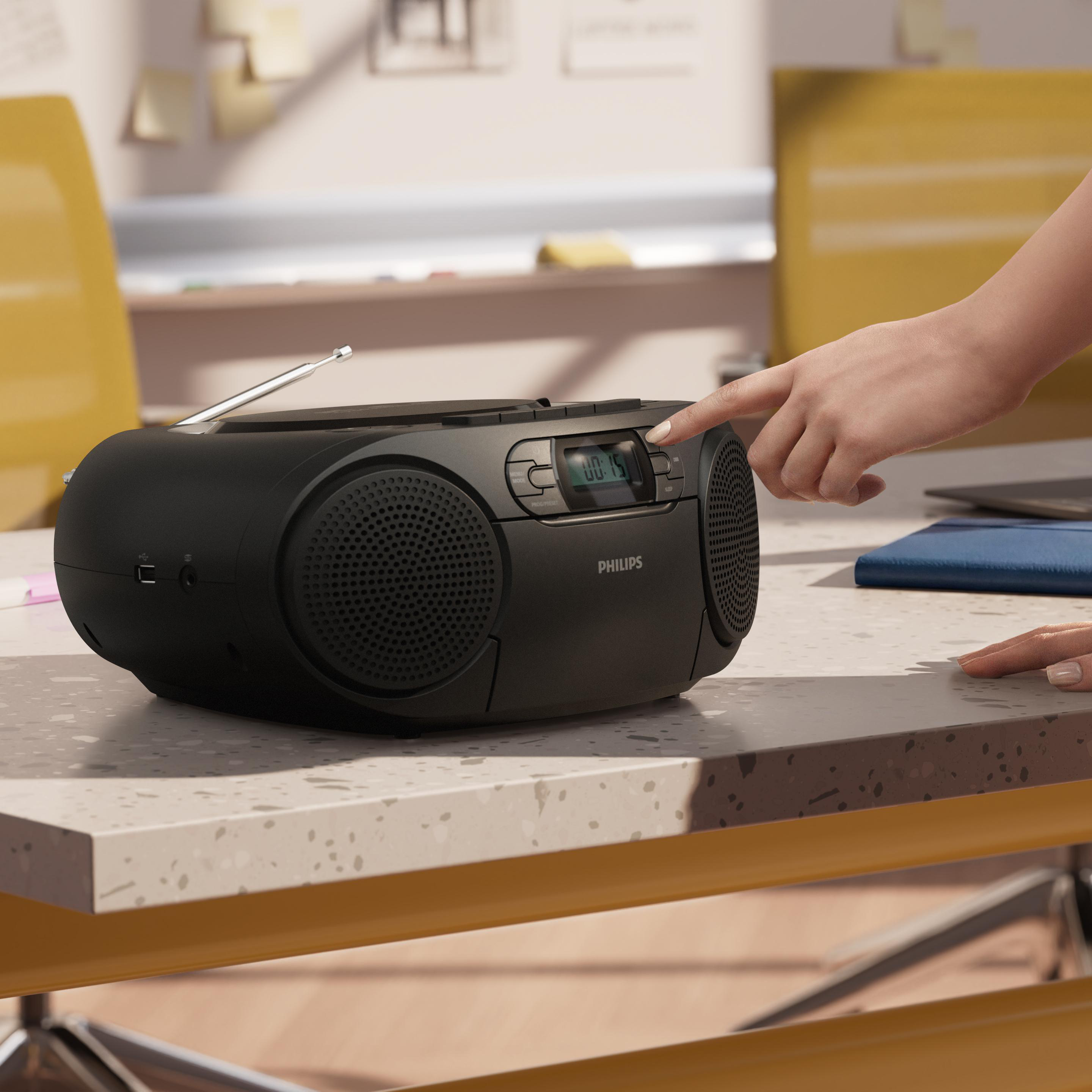Eine Hand bedient die Tasten eines schwarzen Philips-Radios auf einem hellen Tisch in einem Büro.