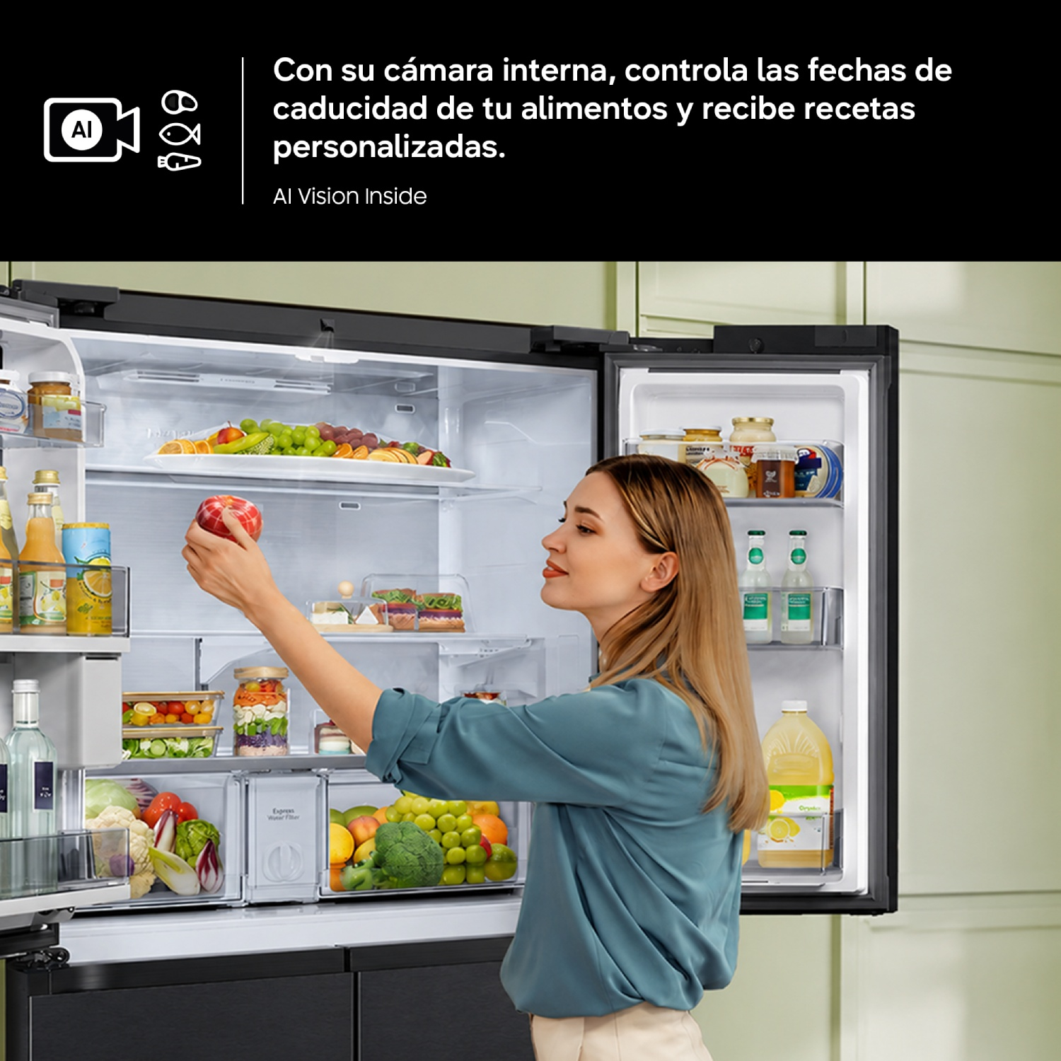 Una mujer con blusa azul toma una manzana roja de un refrigerador grande abierto lleno de comida.