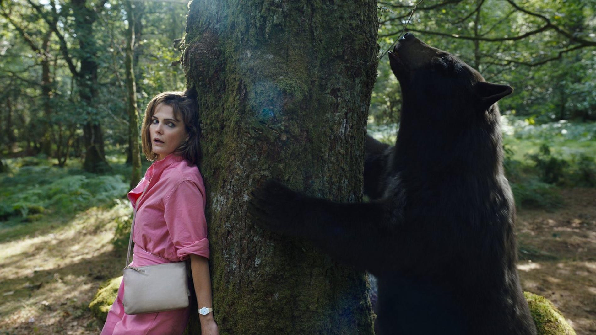 Eine Frau in Rosa lehnt sich an einen Baum, während ein Bär ihn berührt.
