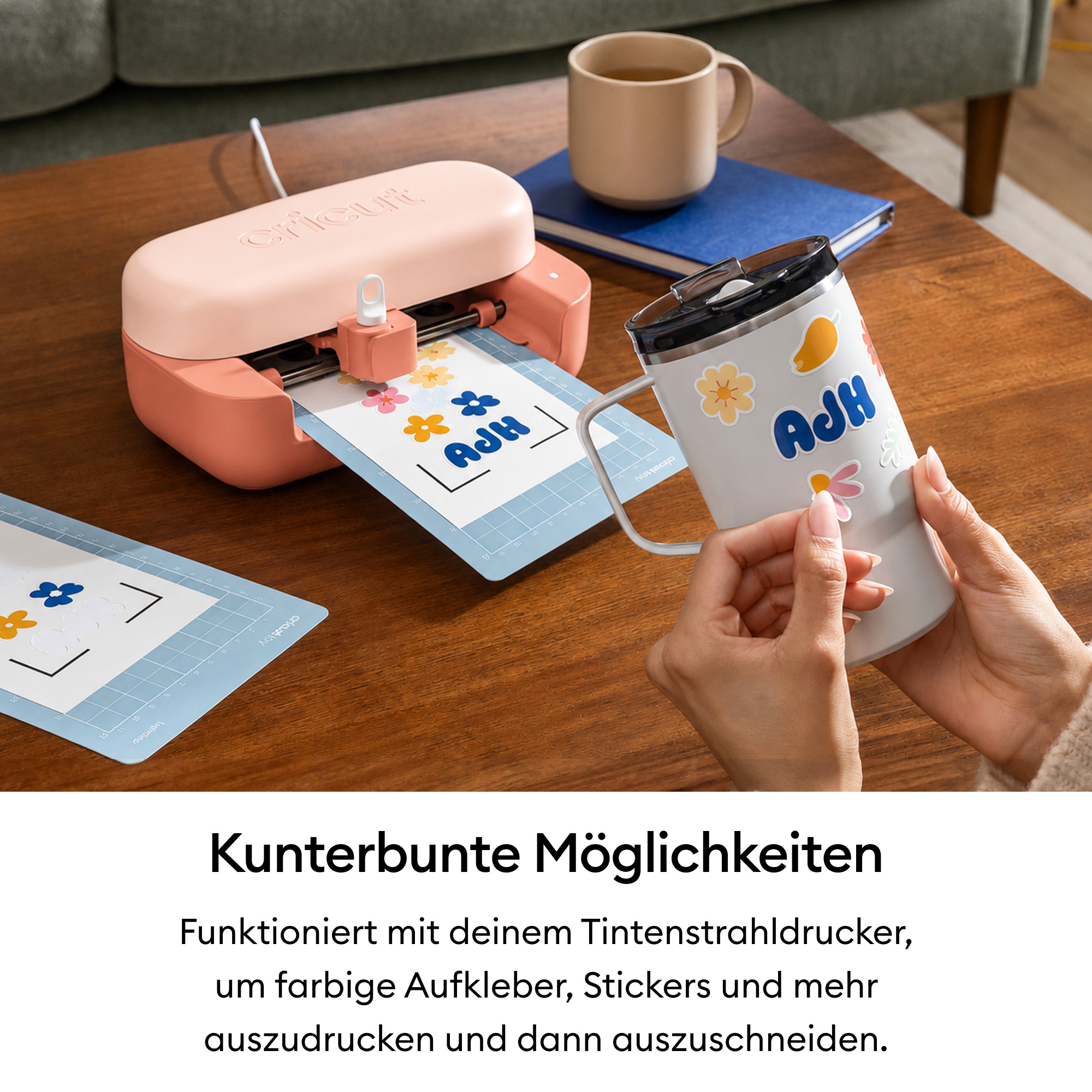 Eine rosafarbene Schneidemaschine schneidet Sticker auf einem Holzisch, Hände bekleben einen Becher.