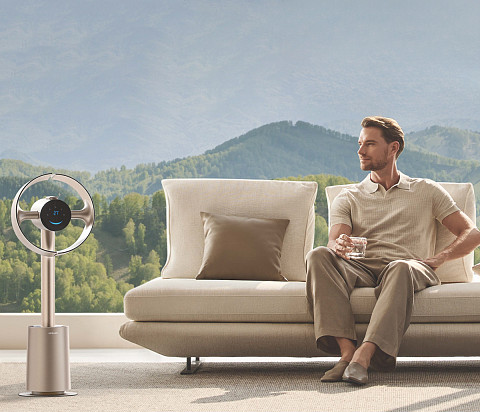 Egy férfi kanapén ül egy ventilátor mellett, háttérben hegyekkel.