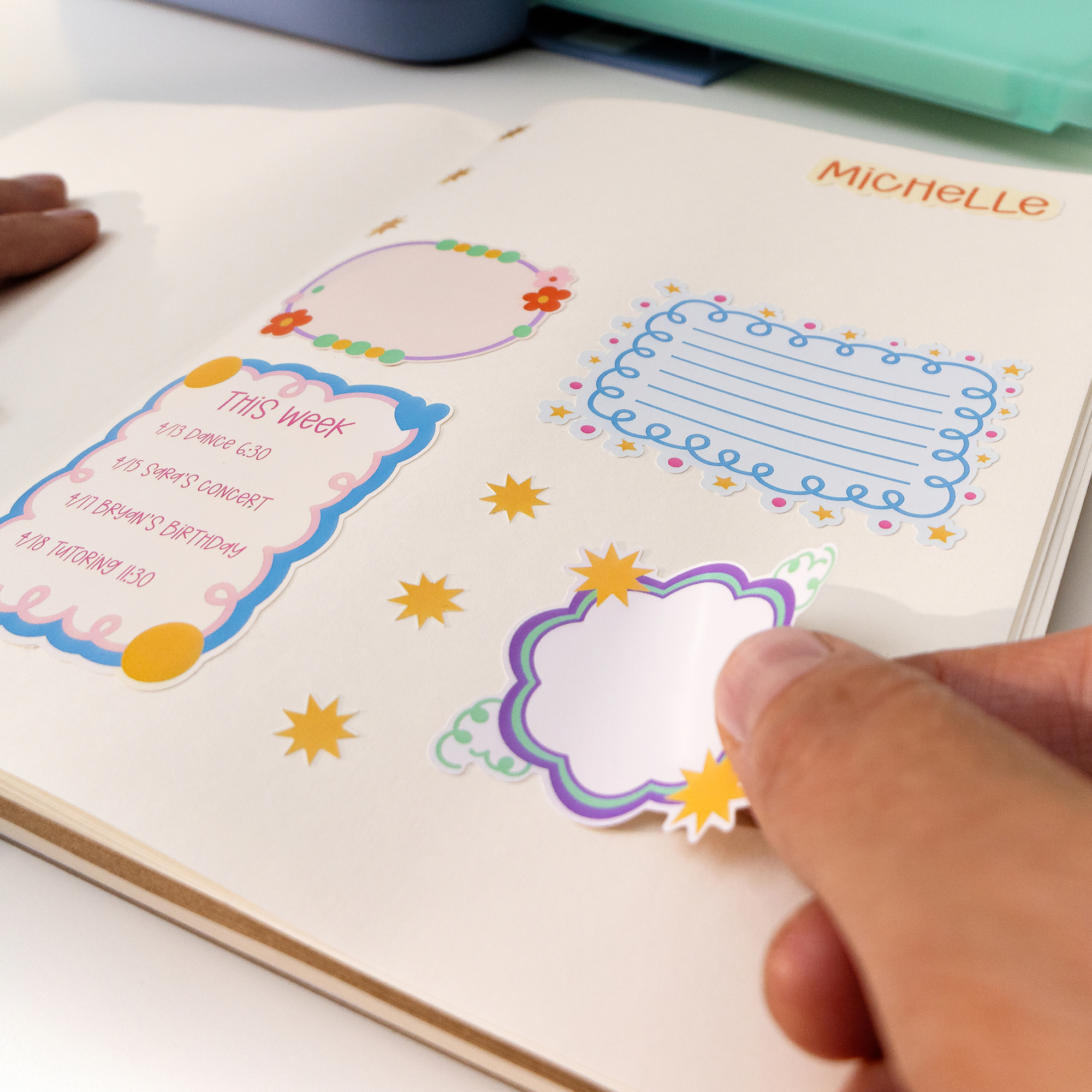 Una mano despega una pegatina colorida dentro de un cuaderno abierto.
