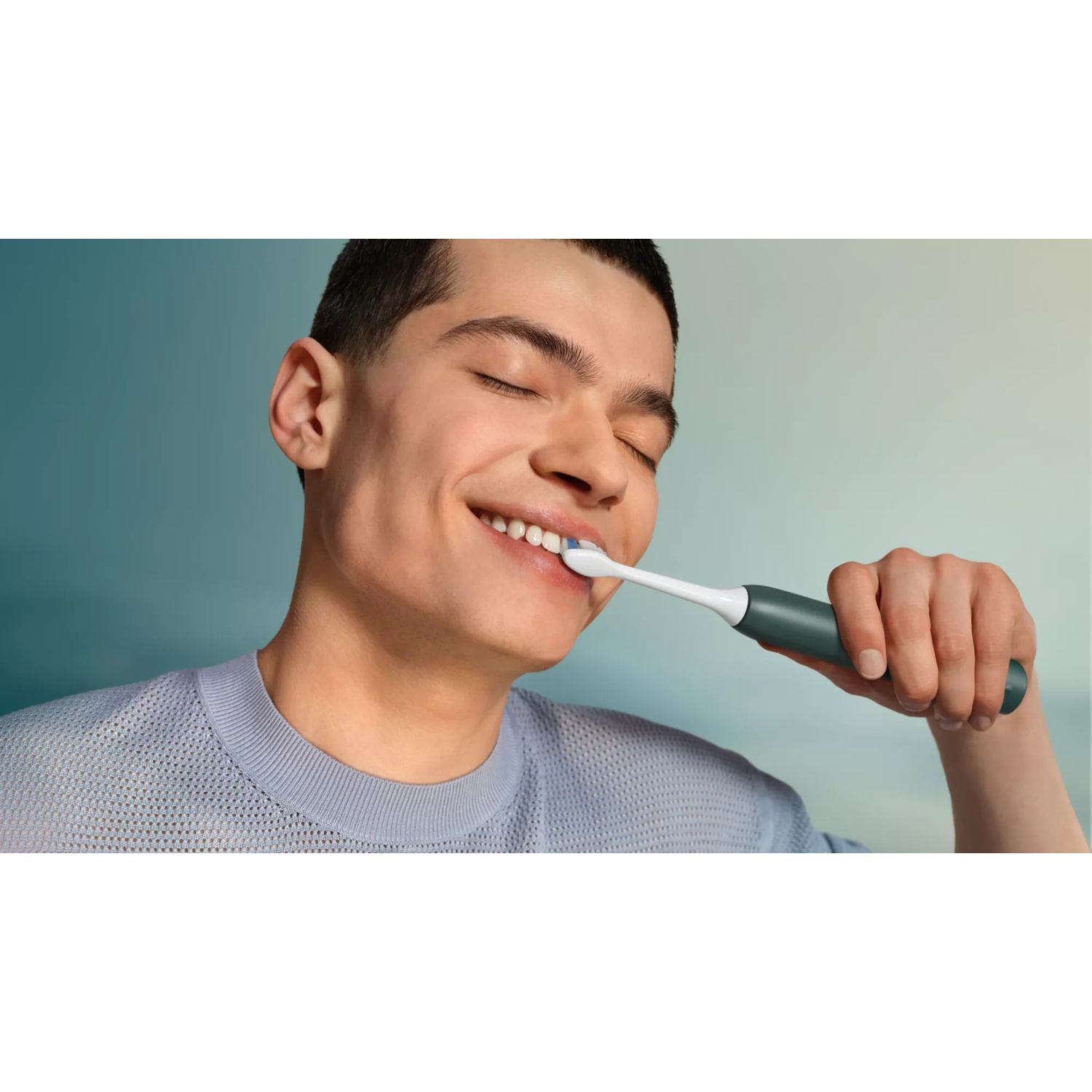 Un giovane con gli occhi chiusi si lava i denti con uno spazzolino elettrico.