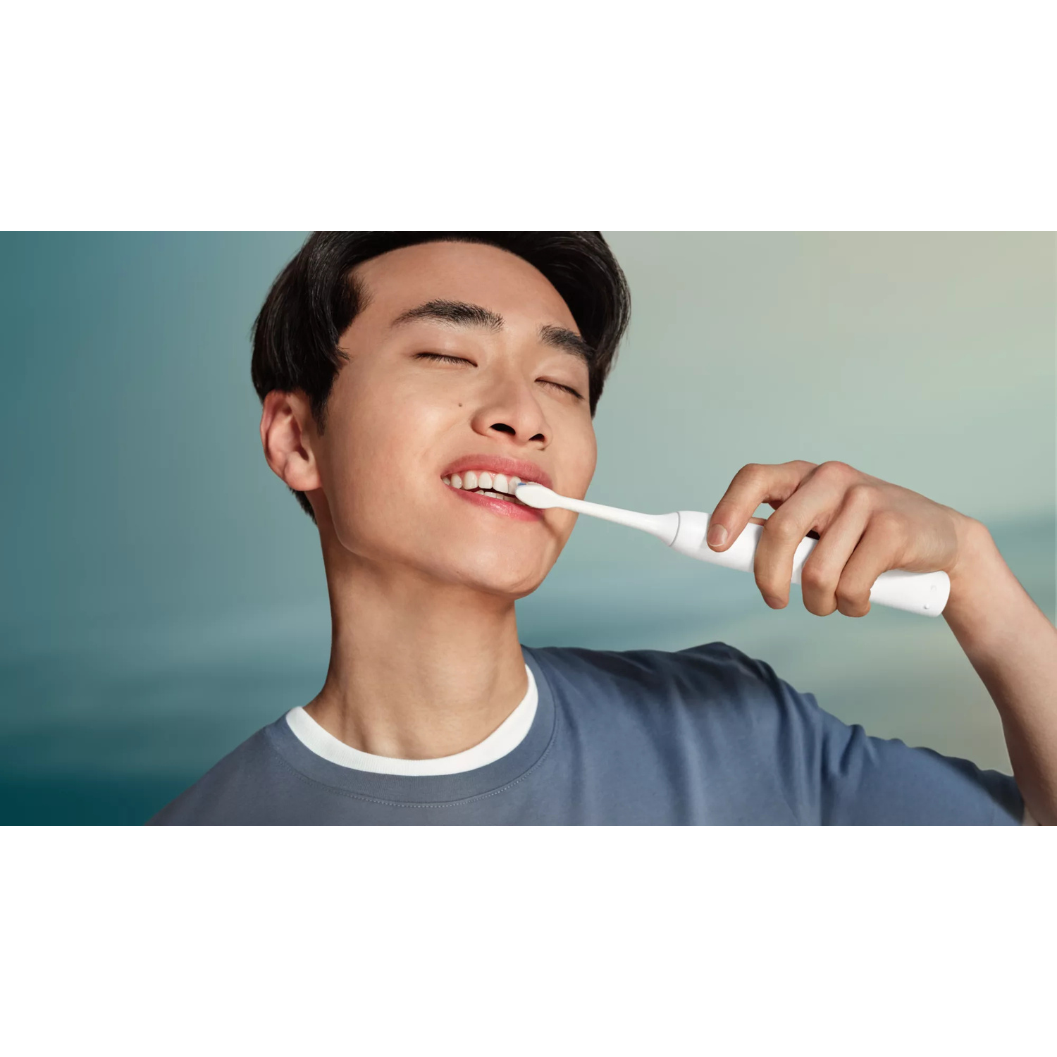 Un giovane con gli occhi chiusi si lava i denti con uno spazzolino elettrico bianco.