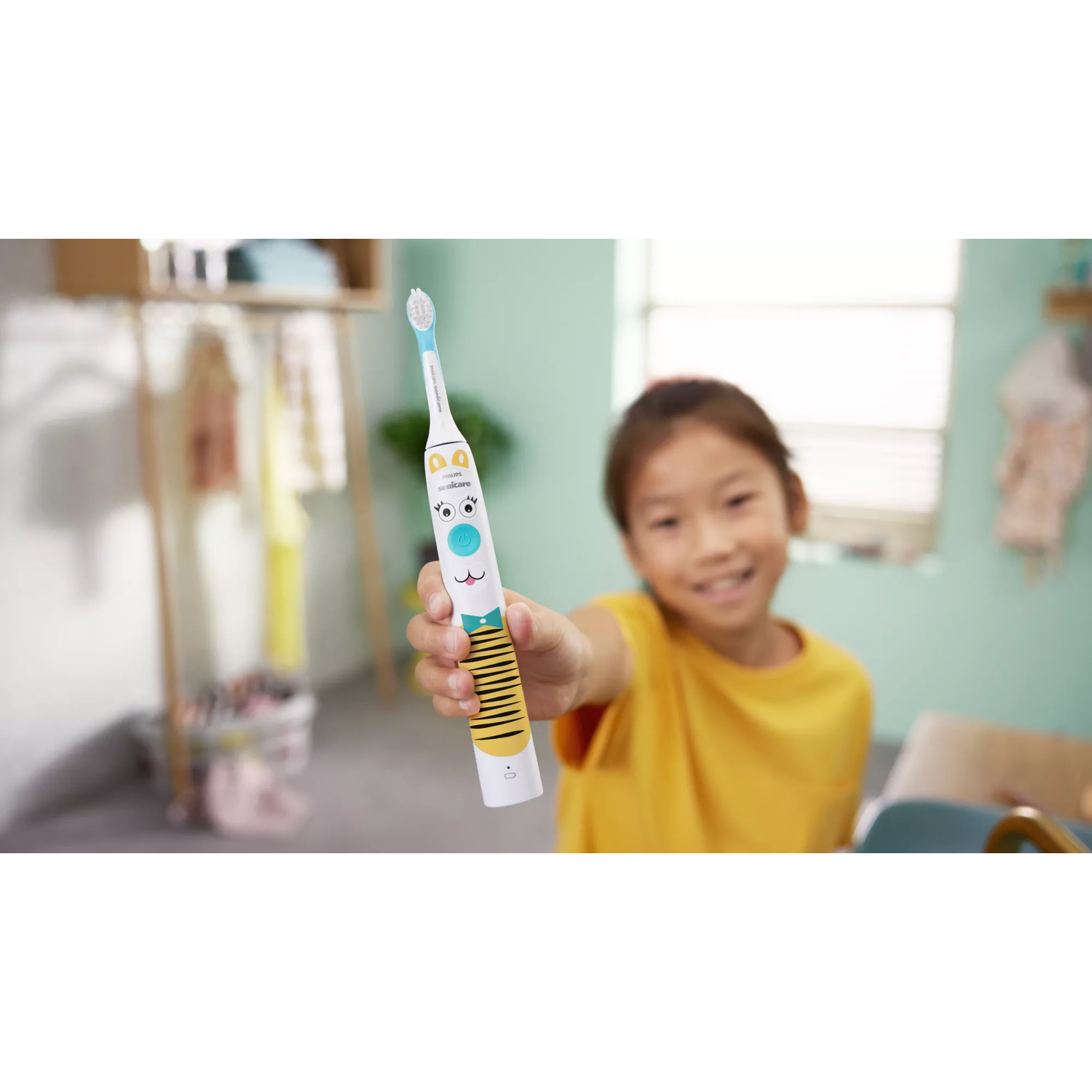Una bambina sorridente con una maglietta gialla mostra uno spazzolino elettrico.