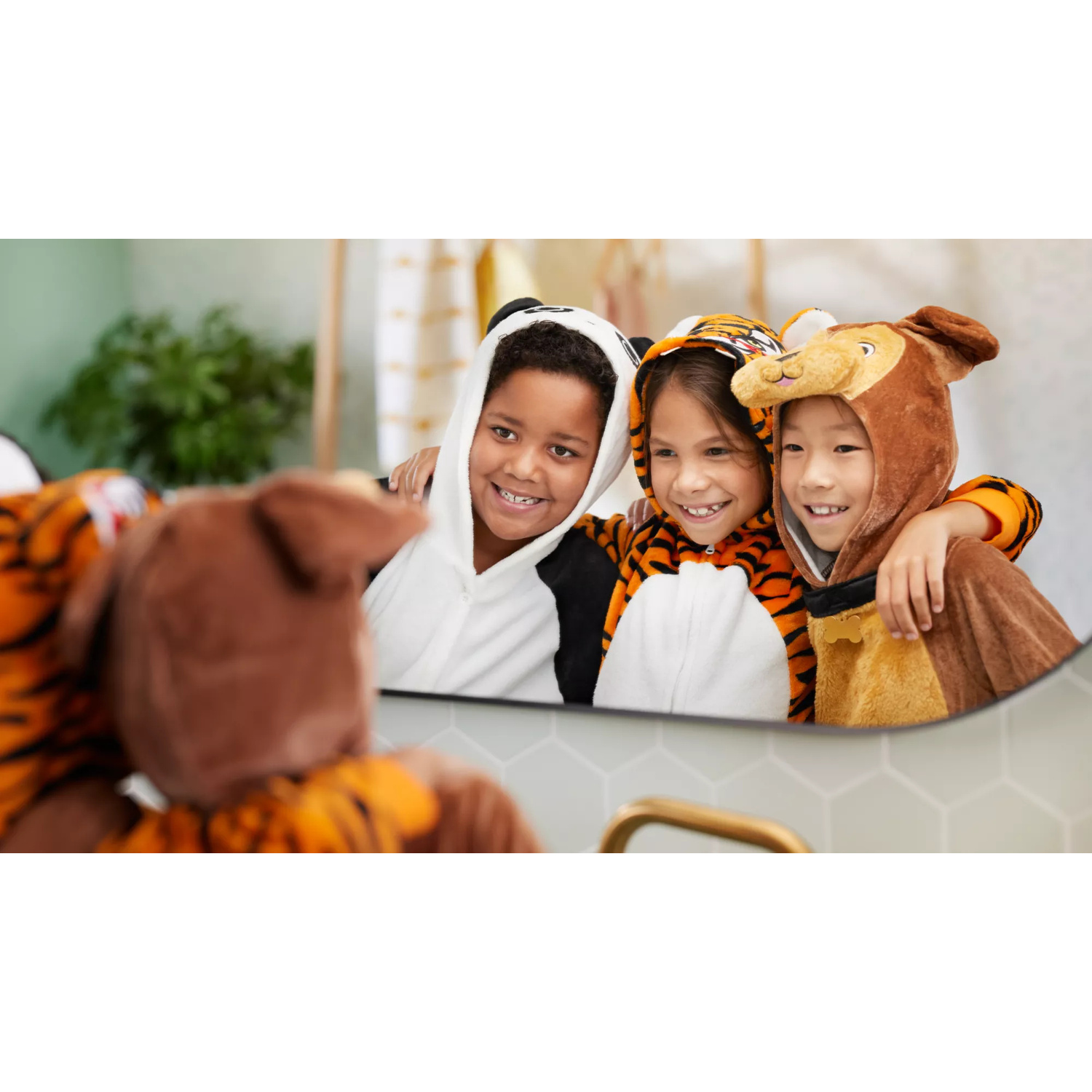 Tre bambini in pigiama da animale sorridono guardandosi allo specchio del bagno.