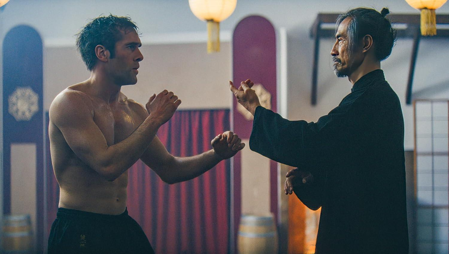 Ein shirtless Kämpfer übt Kampfkunst mit einem älteren Meister in einem Dojo.