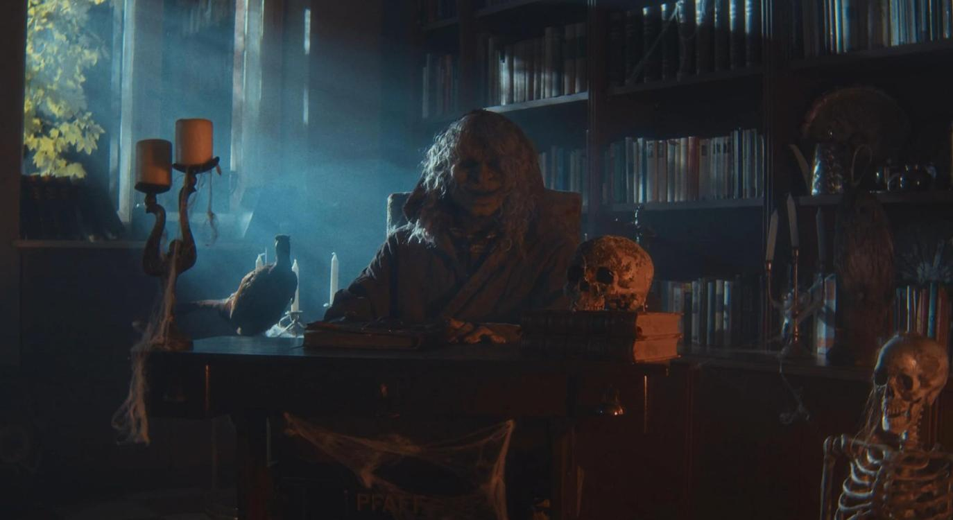 Eine gruselige Figur mit Totenkopf auf einem Schreibtisch in einer dunklen, nebligen Bibliothek.
