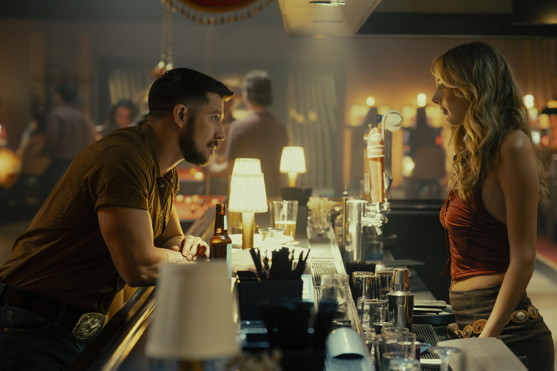 Ein Mann und eine Frau stehen sich in einer Bar an einer Theke gegenüber und unterhalten sich.