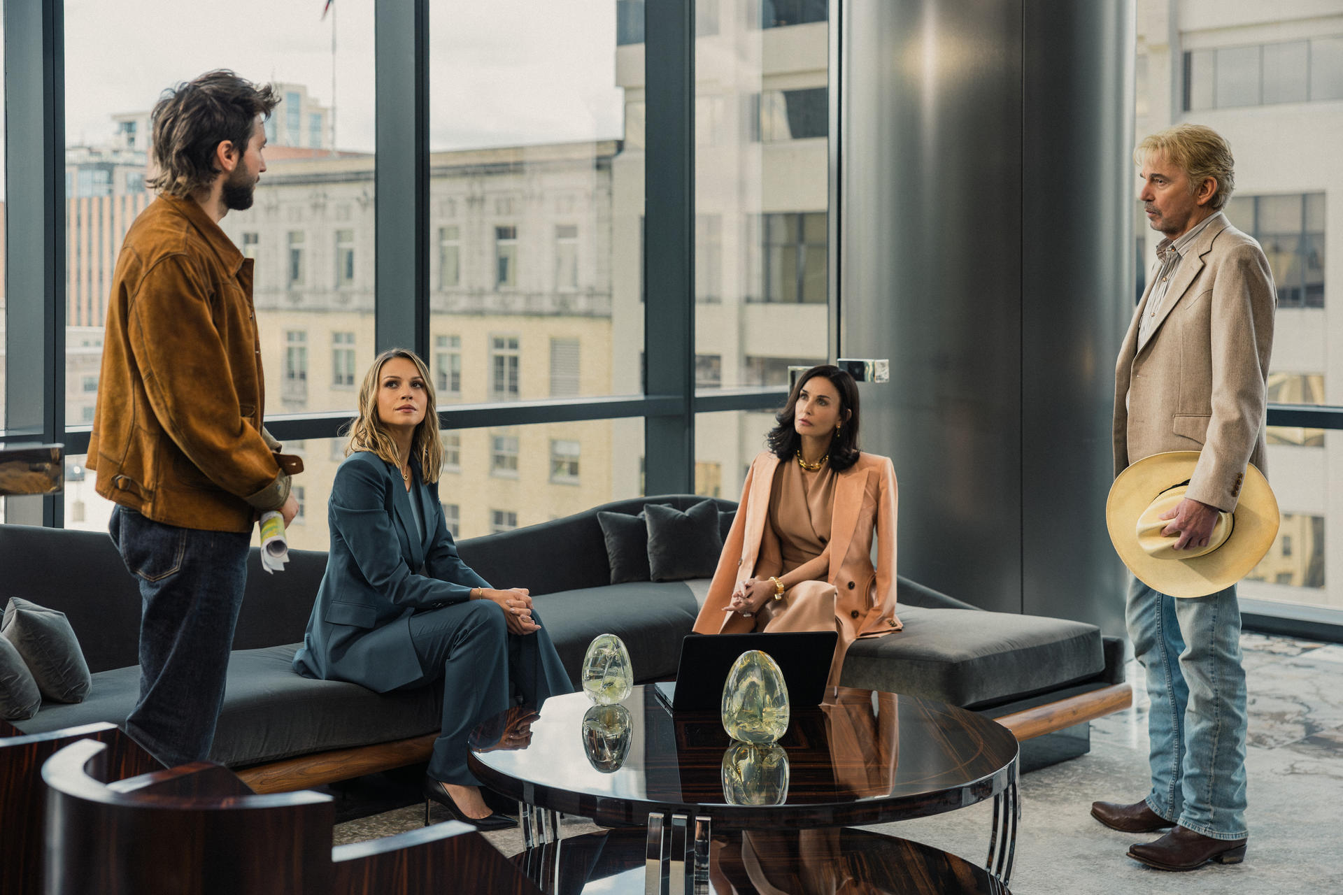 Vier Personen versammeln sich in einem modernen Büro mit großen Fenstern und besprechen Geschäfte.
